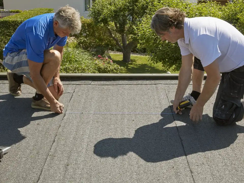 Due persone che lavorano su un tetto piano e misurano lo spazio da ricavare per installare una finestra per tetti piani VELUX..