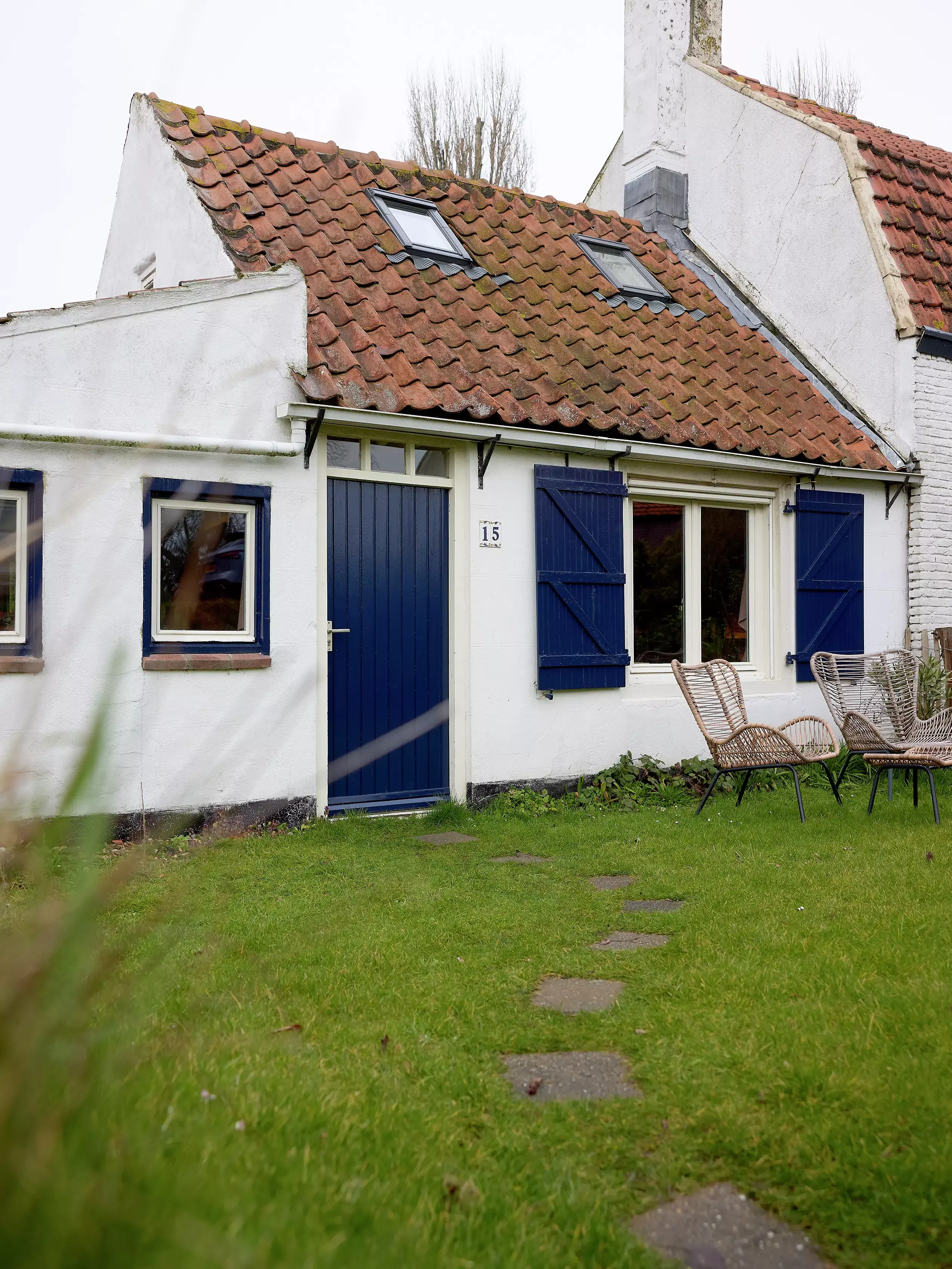 Cottage traditionnel en terrasse avec toit en tuiles rouges et fenêtres VELUX, murs blancs et accents bleus.