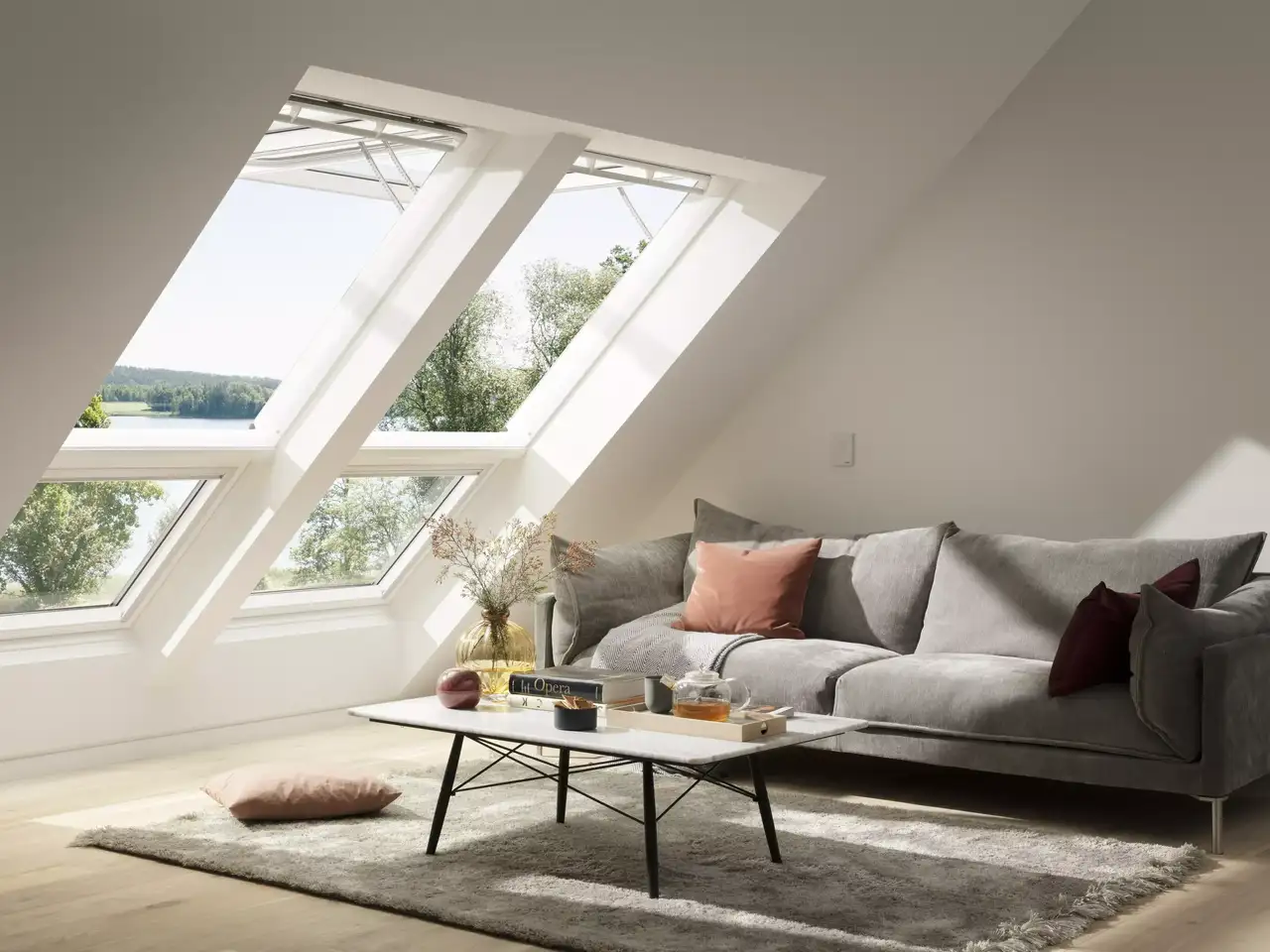 Gemütliches Wohnzimmer im Dachboden mit VELUX Dachflächenfenstern und einem grauen Sofa.