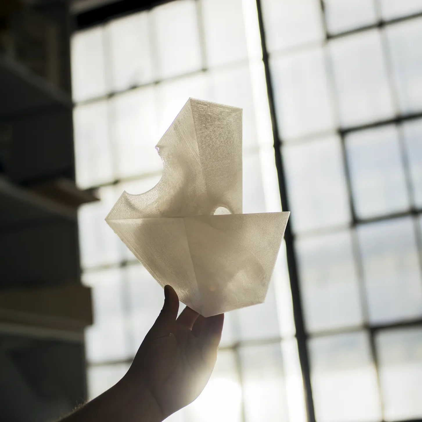 Hand holding a translucent abstract sculpture in front of a large window.