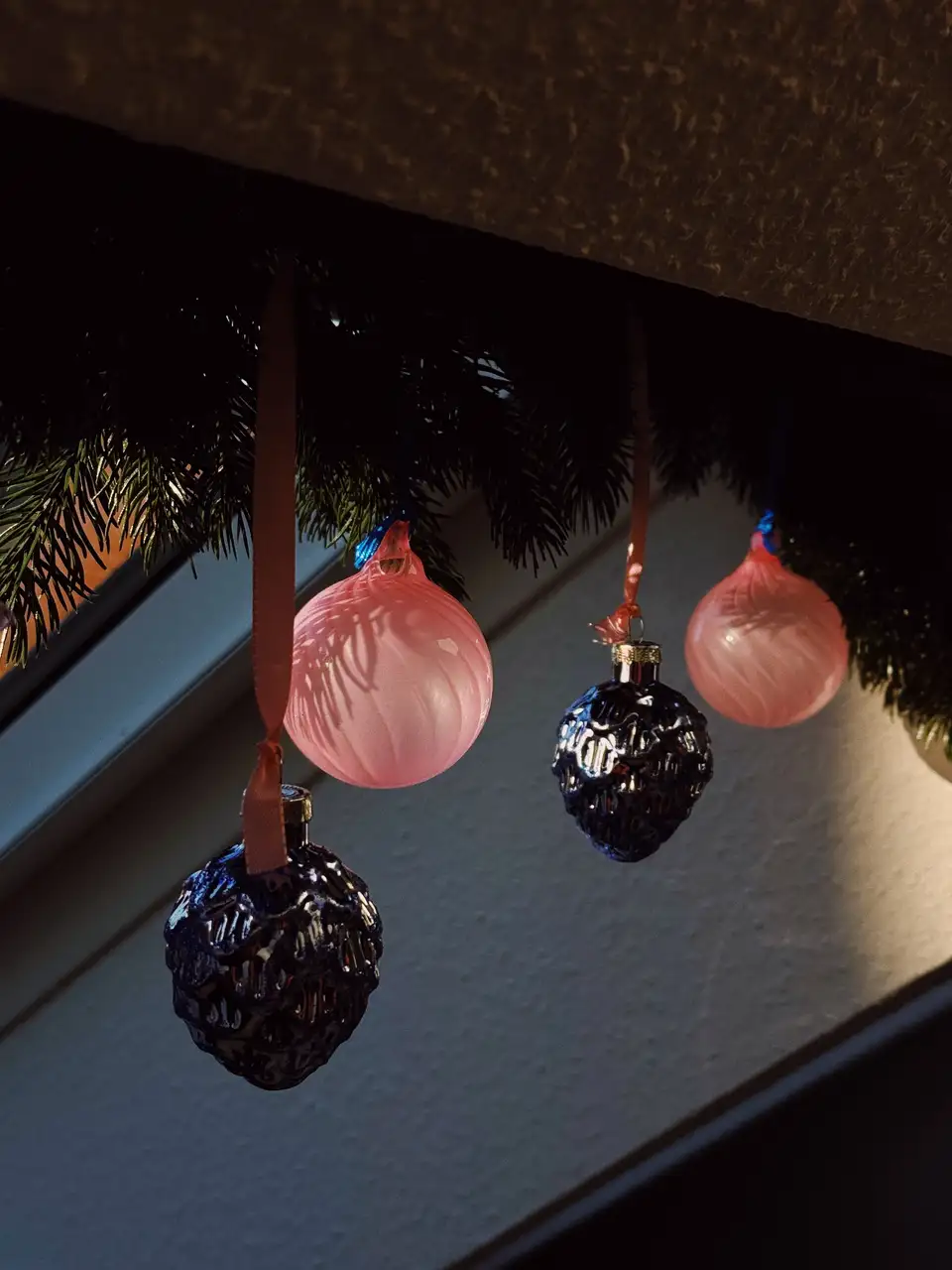 Decorazione natalizia classica con palline rosa e blu appese con nastri a una finestra per tetti VELUX.