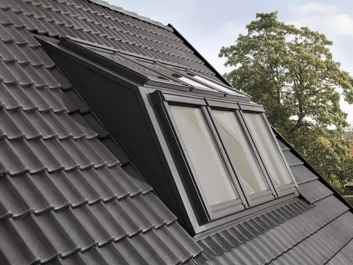 VELUX Dachflächenfenster auf einem mit Ziegeln gedeckten geneigten Dach mit Aussicht auf Bäume.