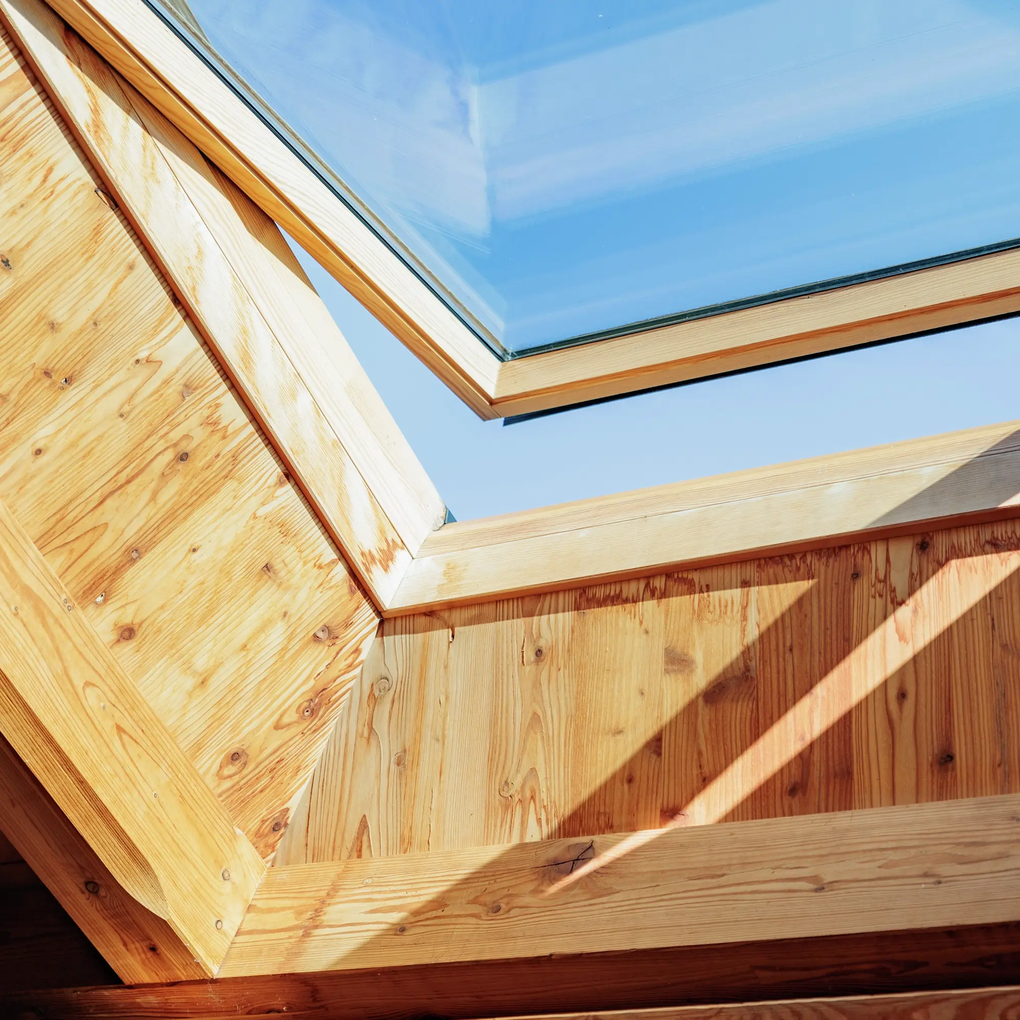 Fenêtre de toit VELUX illuminant un intérieur de comble en bois avec de la lumière naturelle.