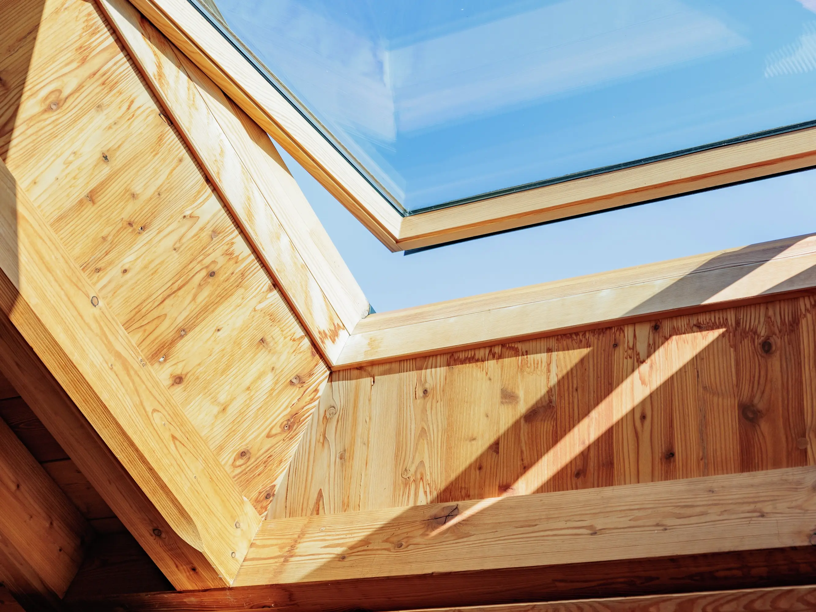 Fenêtre de toit VELUX dans un grenier en bois, apportant de la lumière du soleil et une vue sur le ciel bleu.