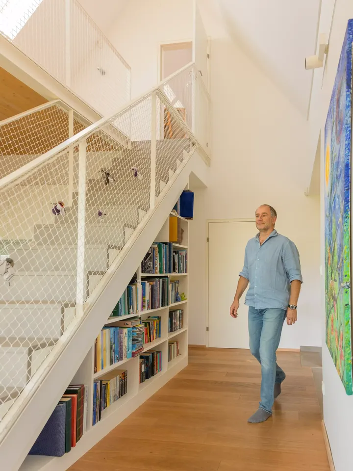 Mann durchquert Flur mit Wandgemälde, weißer Gittertreppe zur offenen Galerie und integriertem Bücherregal | VELUX 