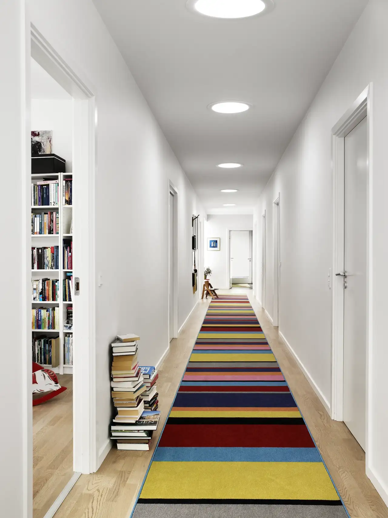 Couloir blanc avec passéia rayée multicolore qui apporte dynamisme et allonge visuellement l’espace.