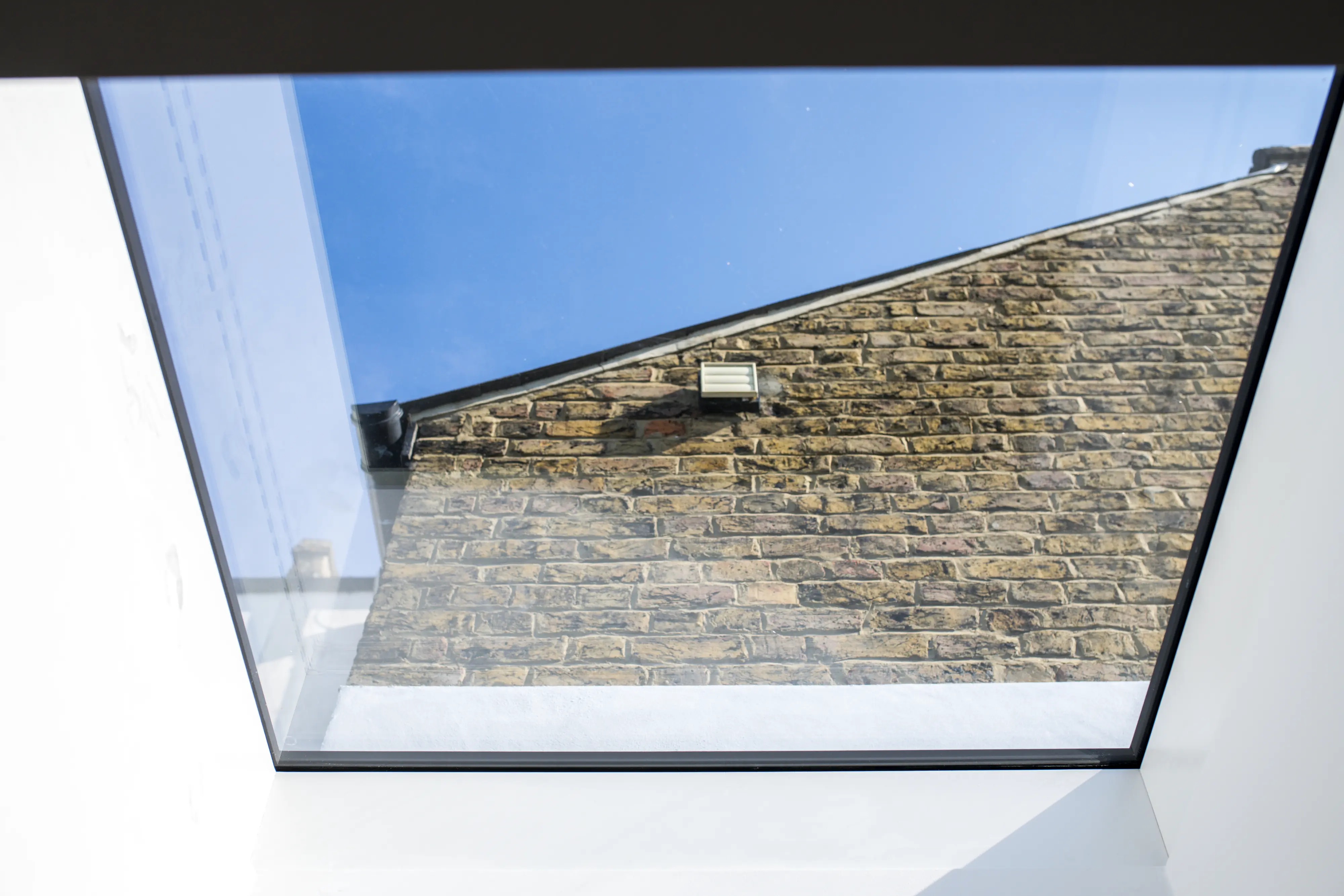View through VELUX roof window showing brick building and blue sky.