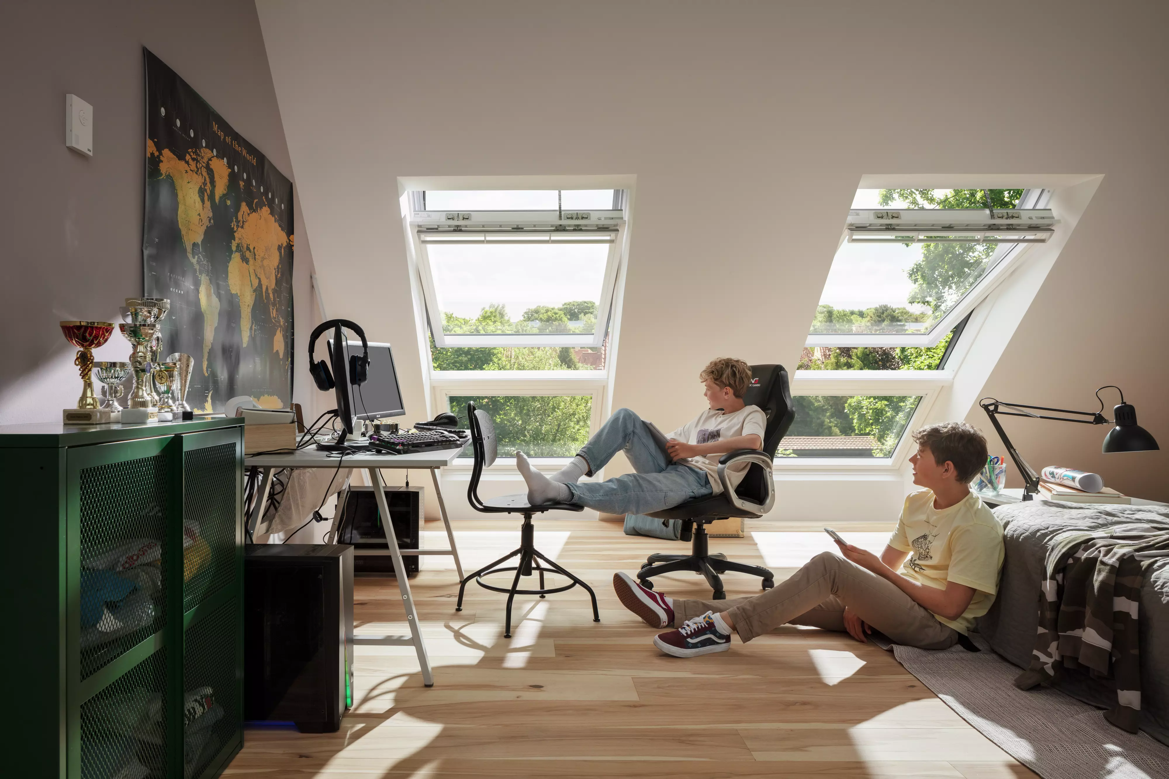 Chambre d'adolescent avec des fenêtres de toit VELUX, un bureau d'étude, un équipement de jeu, et une carte du monde sur le mur.