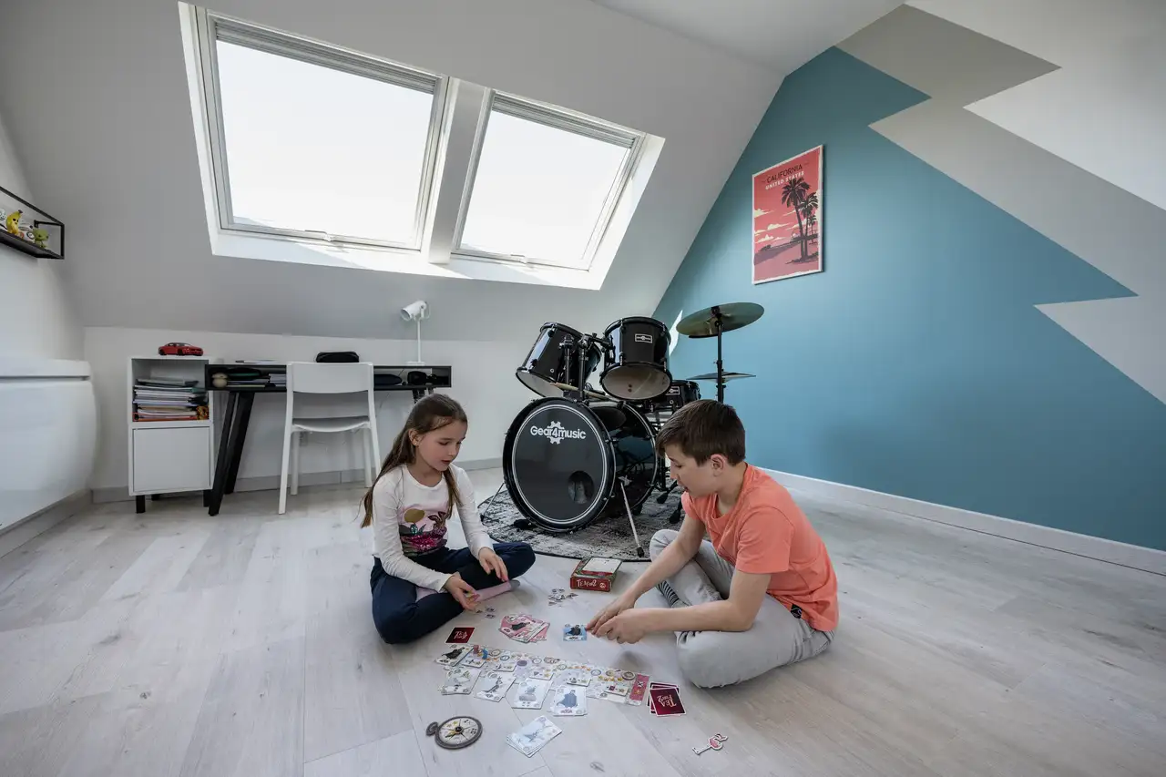 Enfants jouant dans une chambre mansardée avec deux fenêtres de toit