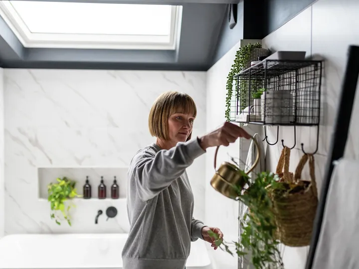 Frau gießt Hängepflanzen im Badezimmer mit  Messing-Gießkanne | VELUX Magazin