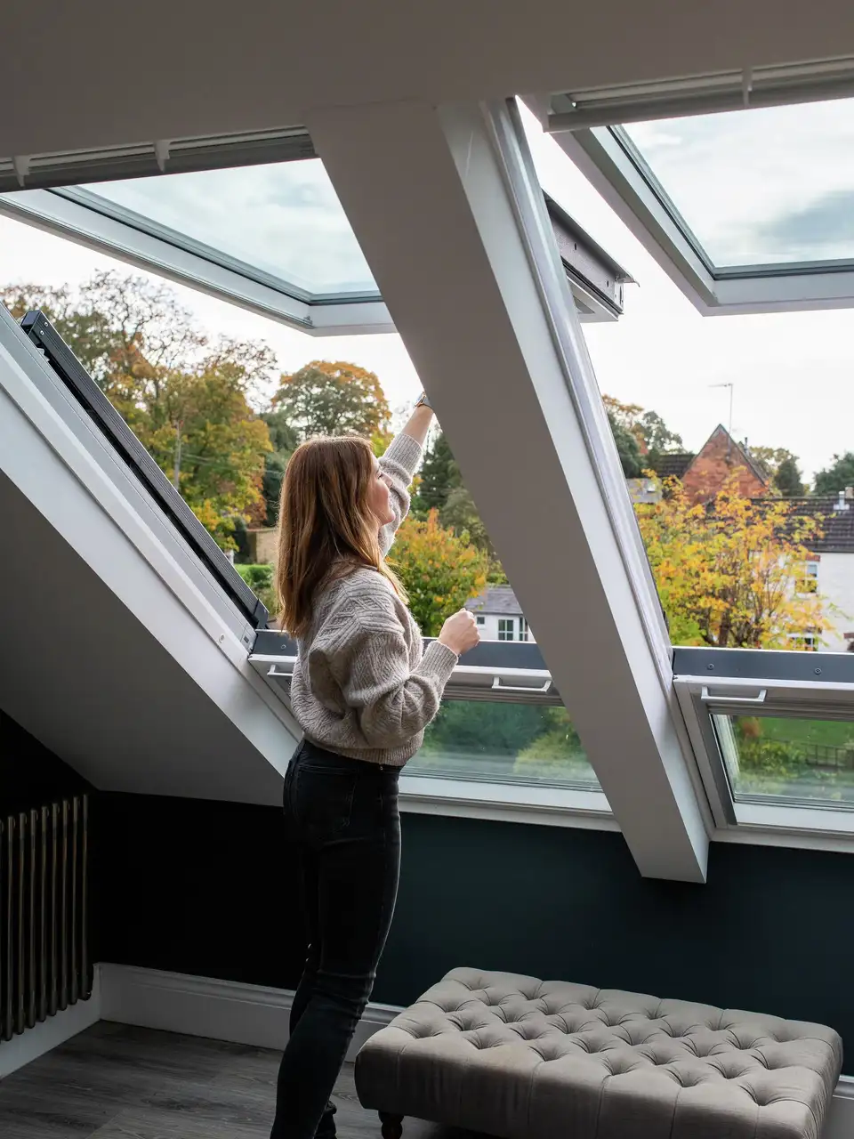 Een vrouw opent een VELUX dakvenster in een zolderkamer met een schuin plafond. 