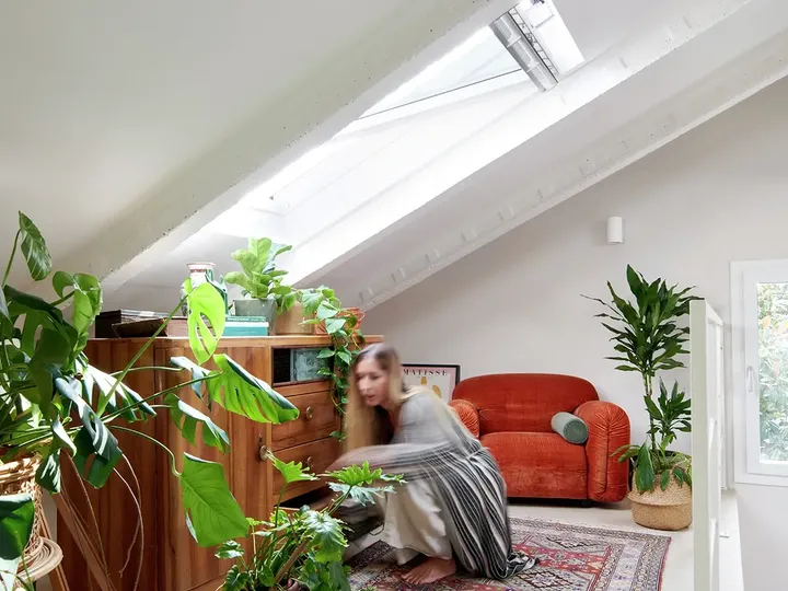 Heller Dachboden-Wohnraum mit VELUX Dachflächenfenstern, hölzernen Möbeln, Pflanzen und orangefarbenem Sofa.