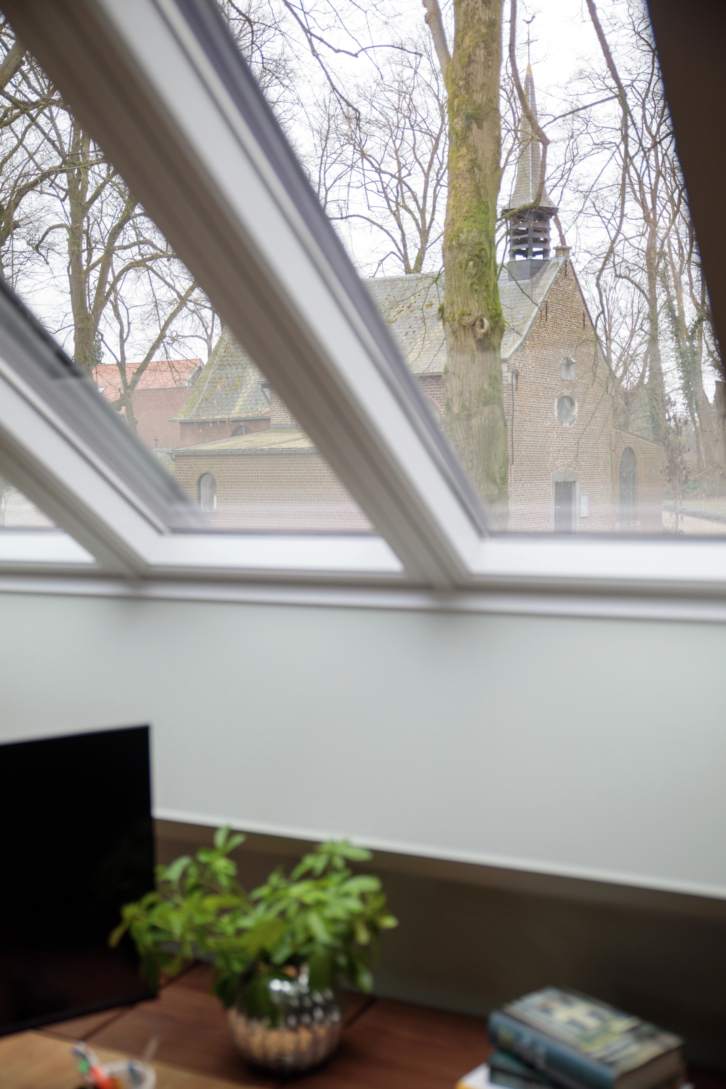 Attic room with VELUX roof window, view of trees and church outside.