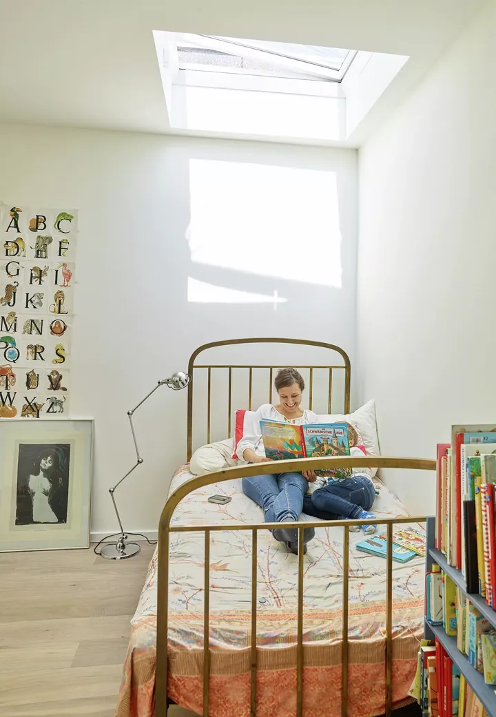 Jugendzimmer mit Bett unter VELUX-Fenster, Bücherregal und Buchstaben-Wandkunst.