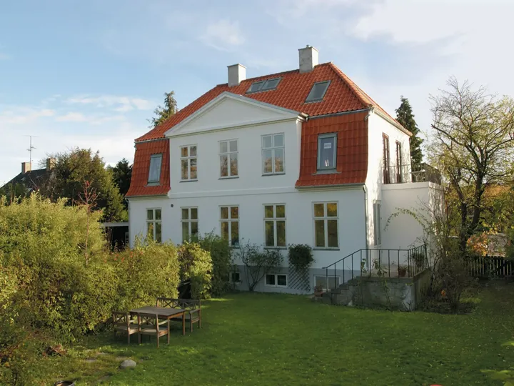 Weißes zweistöckiges Haus mit rotem Dach und VELUX Dachflächenfenster, umgeben von einem grünen Garten.