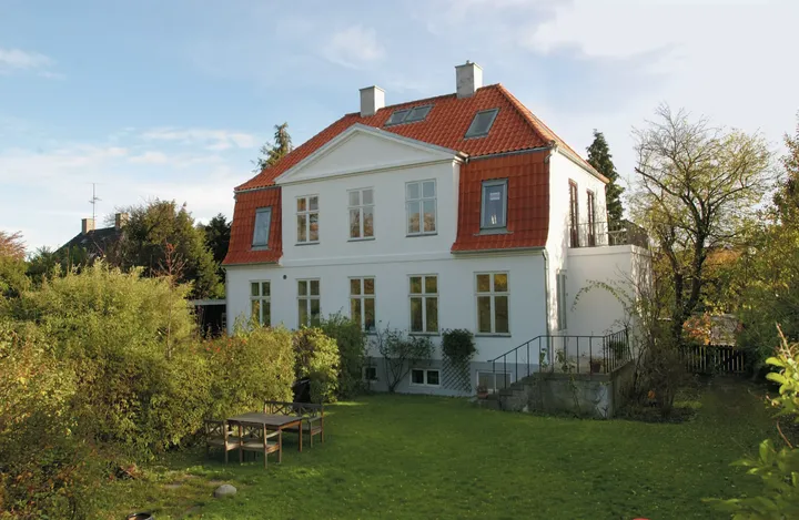 Zweistöckiges weißes Haus mit rotem Dach und VELUX Dachflächenfenstern inmitten von Grünanlagen.