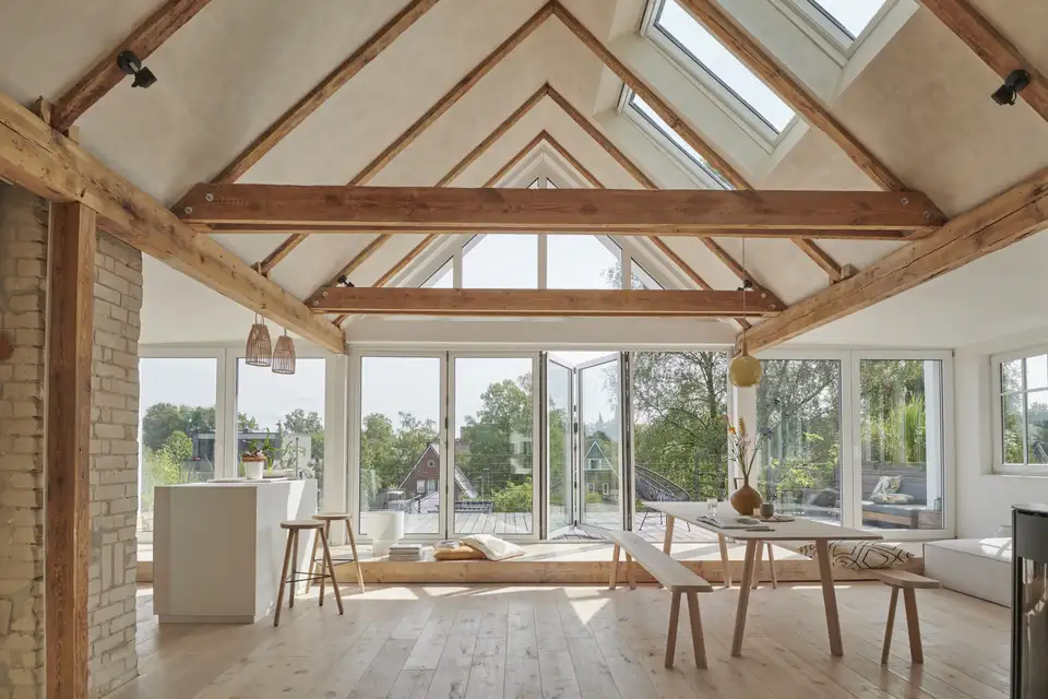 Soggiorno in stile rustico di ispirazione scandinava con travi a vista, pavimento in legno chiaro e grandi finestre.