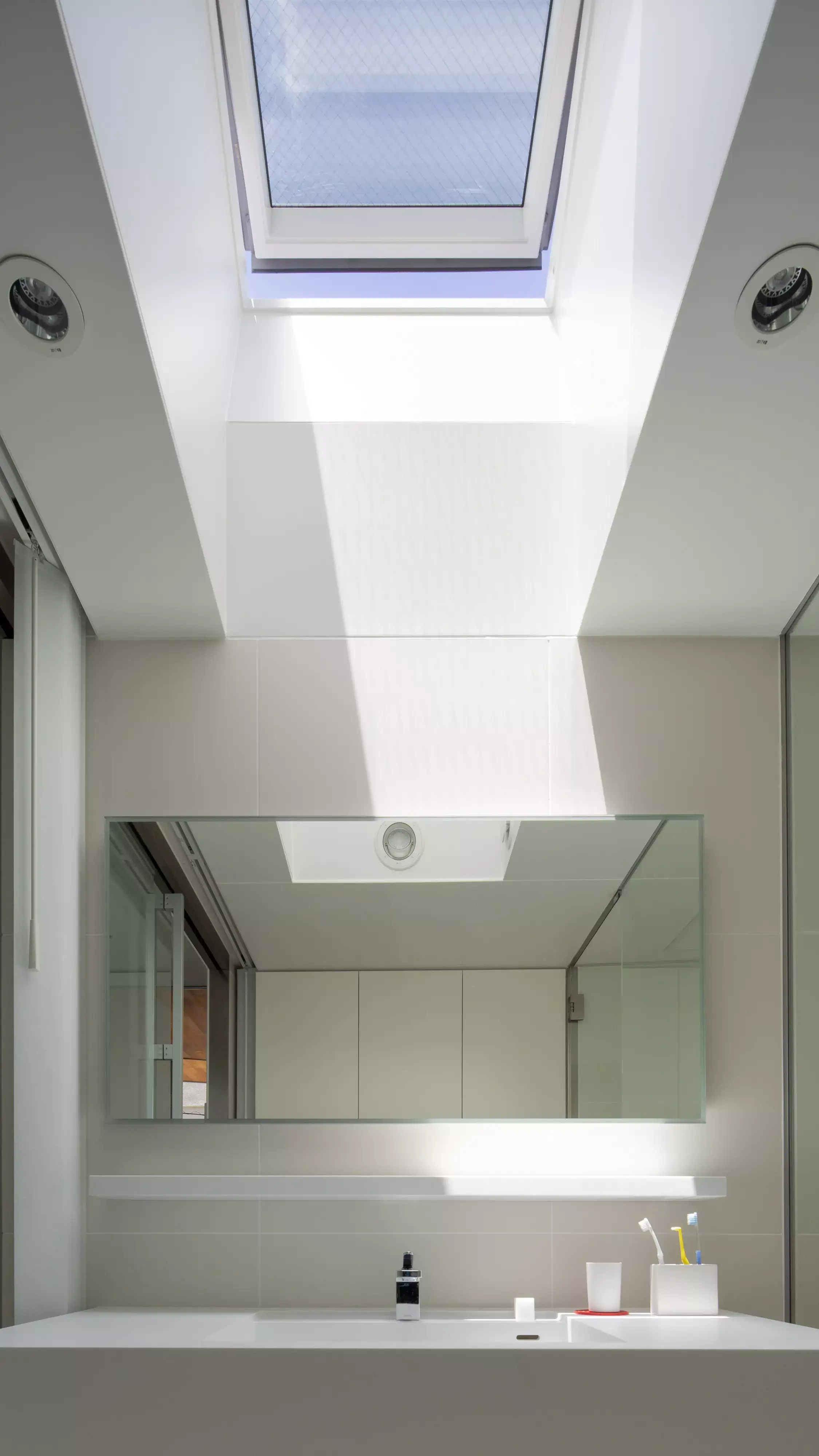 Salle de bain moderne avec lumière naturelle d'une fenêtre de toit VELUX, lavabo blanc et grand miroir.