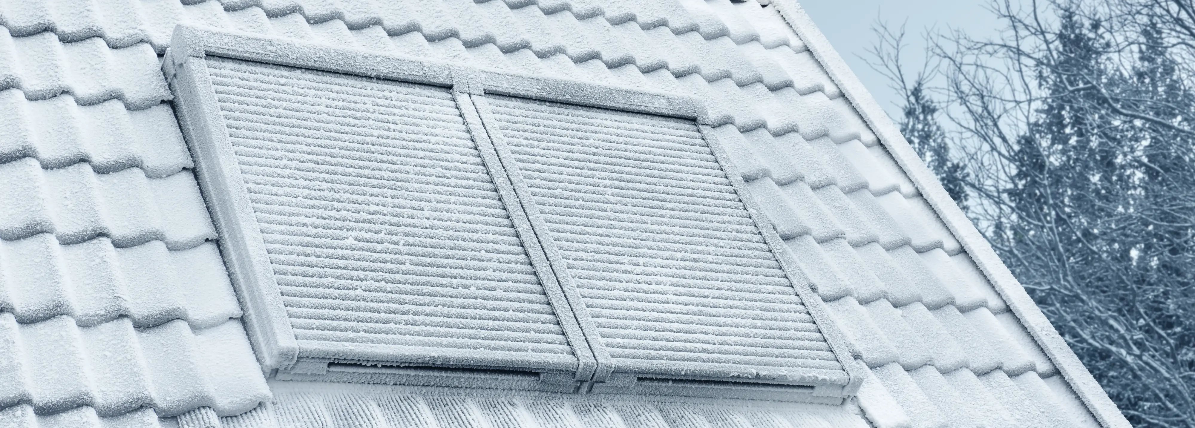 Snow-covered roof with tiles and VELUX roof windows and solar roller shutter.