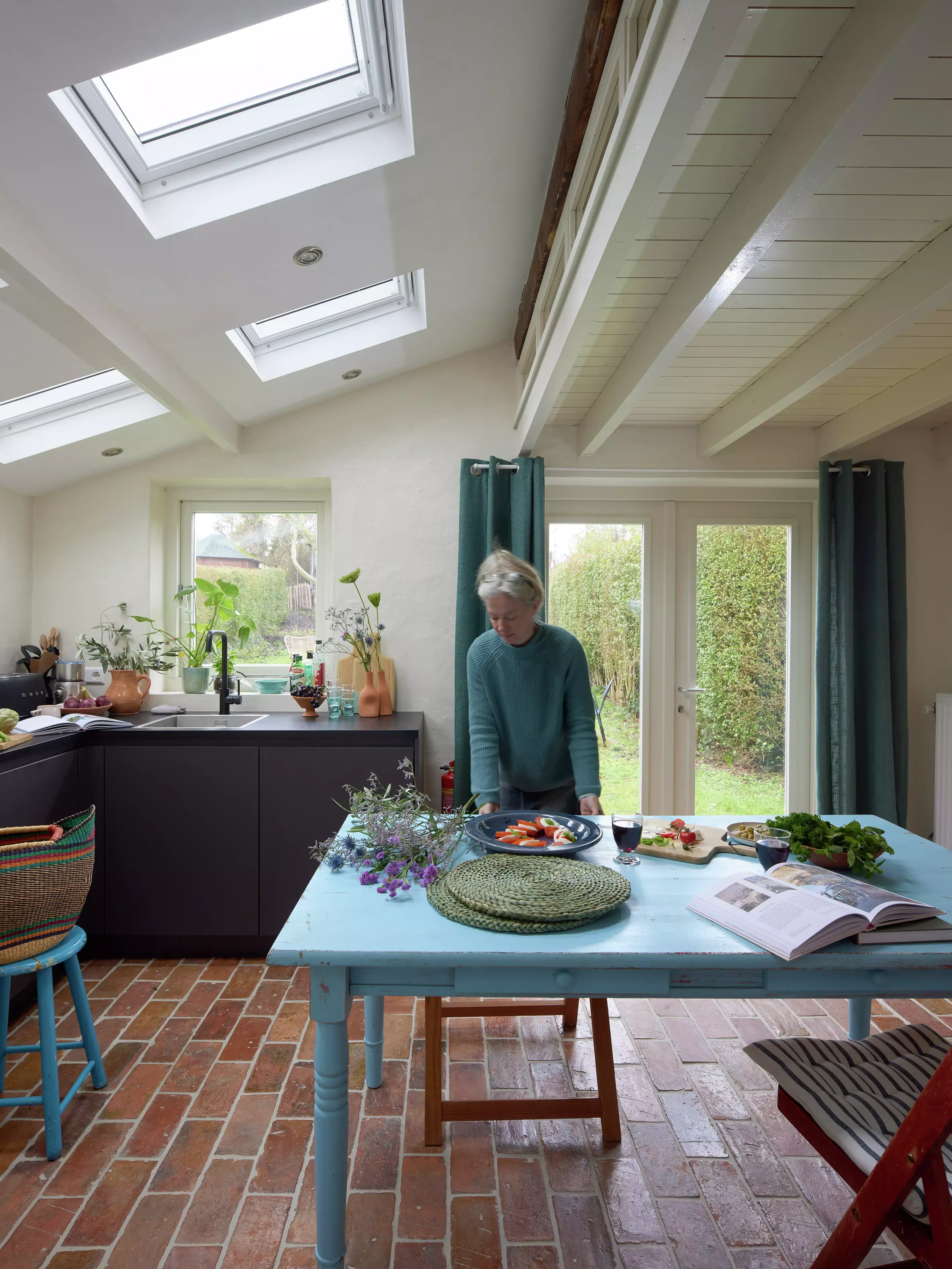 Cuisine confortable avec des carreaux en terre cuite et des fenêtres de toit VELUX au-dessus d'une table bleue.