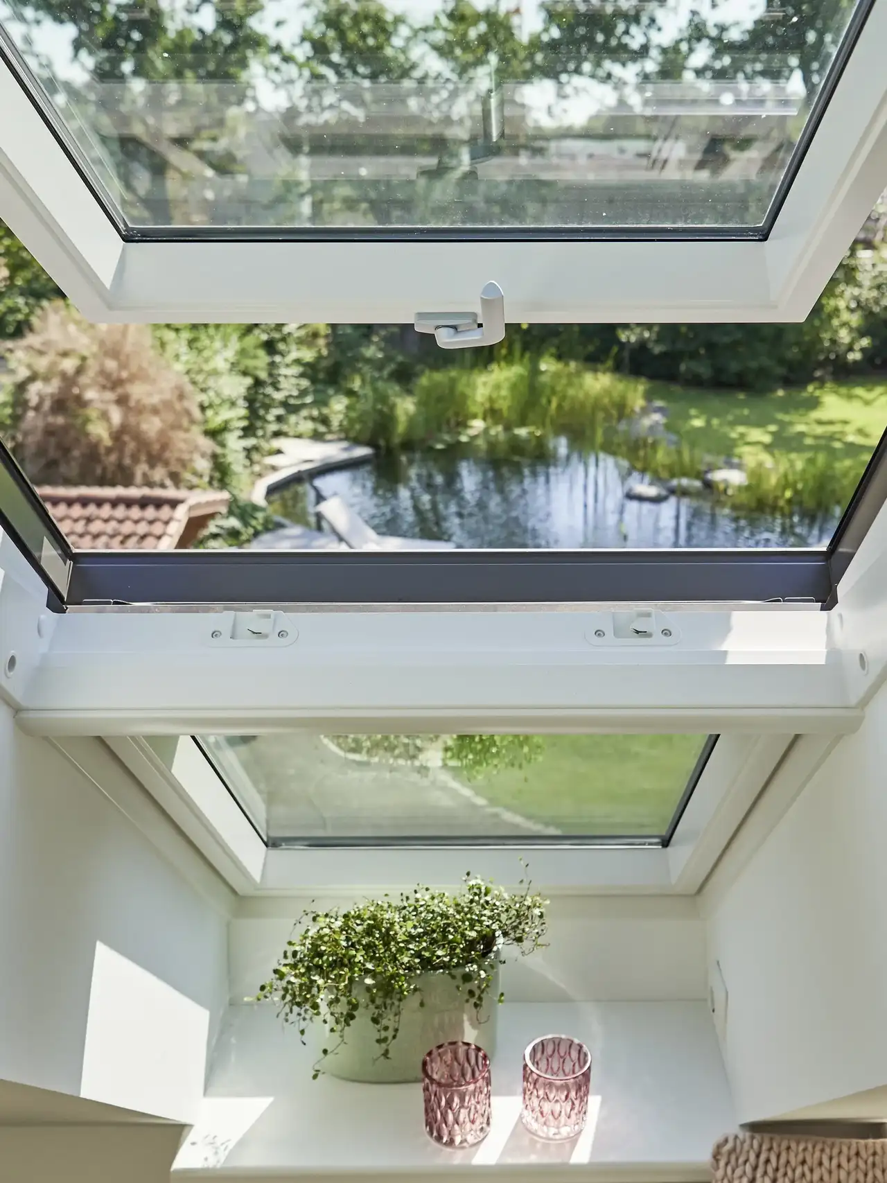 Ventana de tejado abierta para ventilar, con vistas al jardín exterior y al estanque