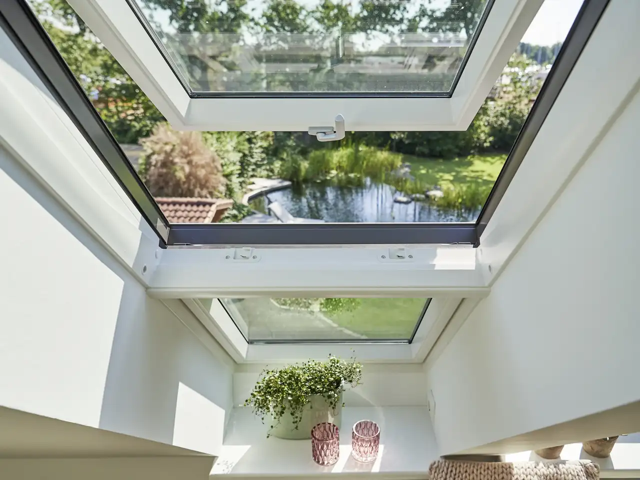 Fenêtre de toit ouverte pour ventiler avec vue sur jardin et bassin extérieur.  