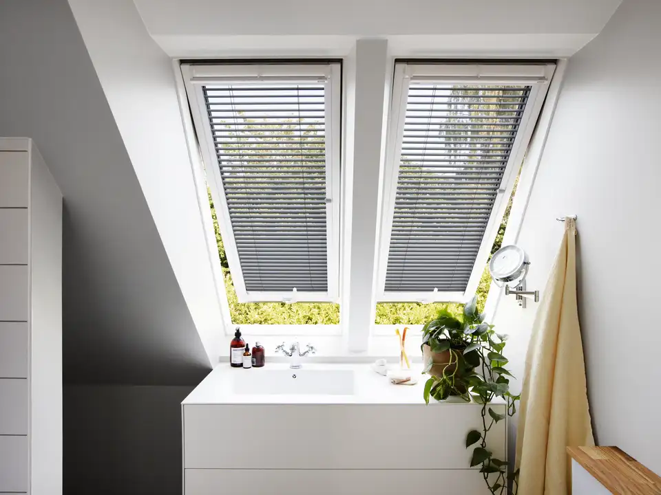 salle de bains mansardée avec deux fenêtres de toit VELUX équipées de stores vénitiens gris
