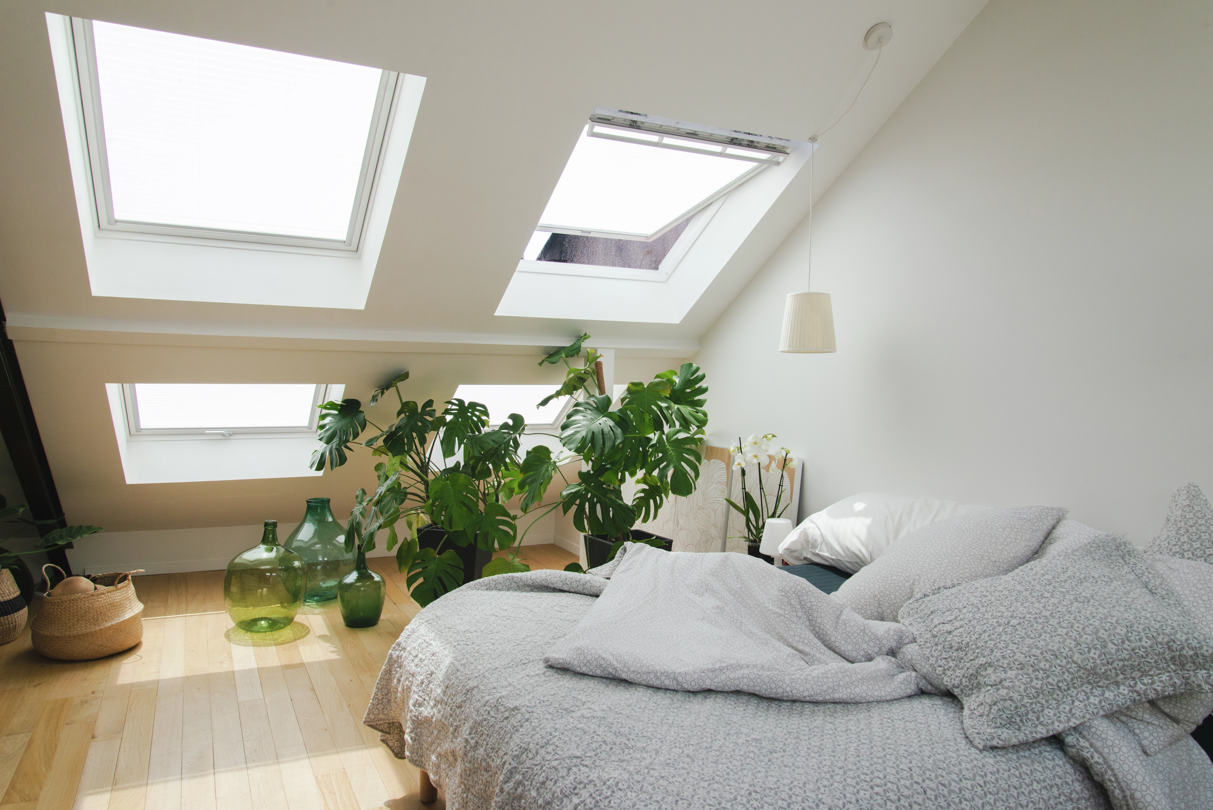 Chambre mansardée lumineuse avec plantes vertes et linge de lit gris.