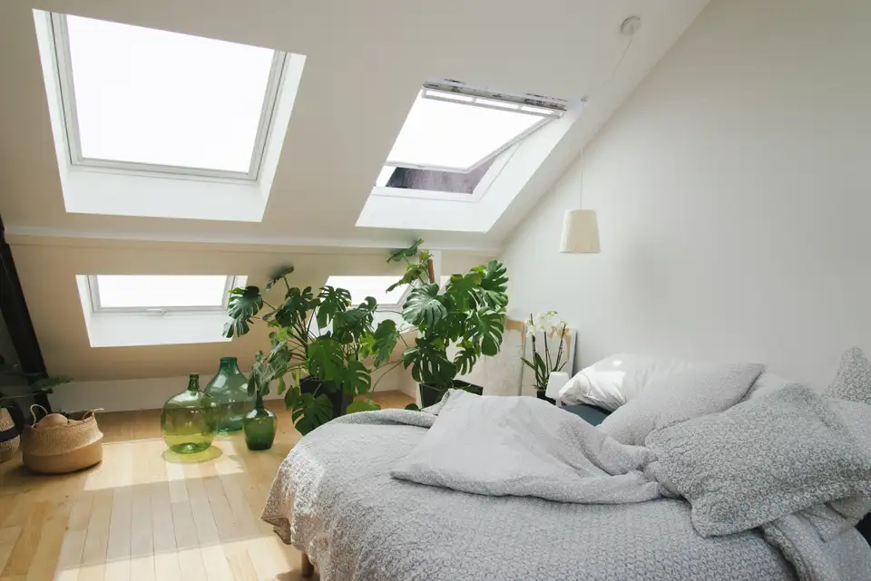 Svetla mansardna spalnica z zelenimi rastlinami in sivo posteljnino. | VELUX 