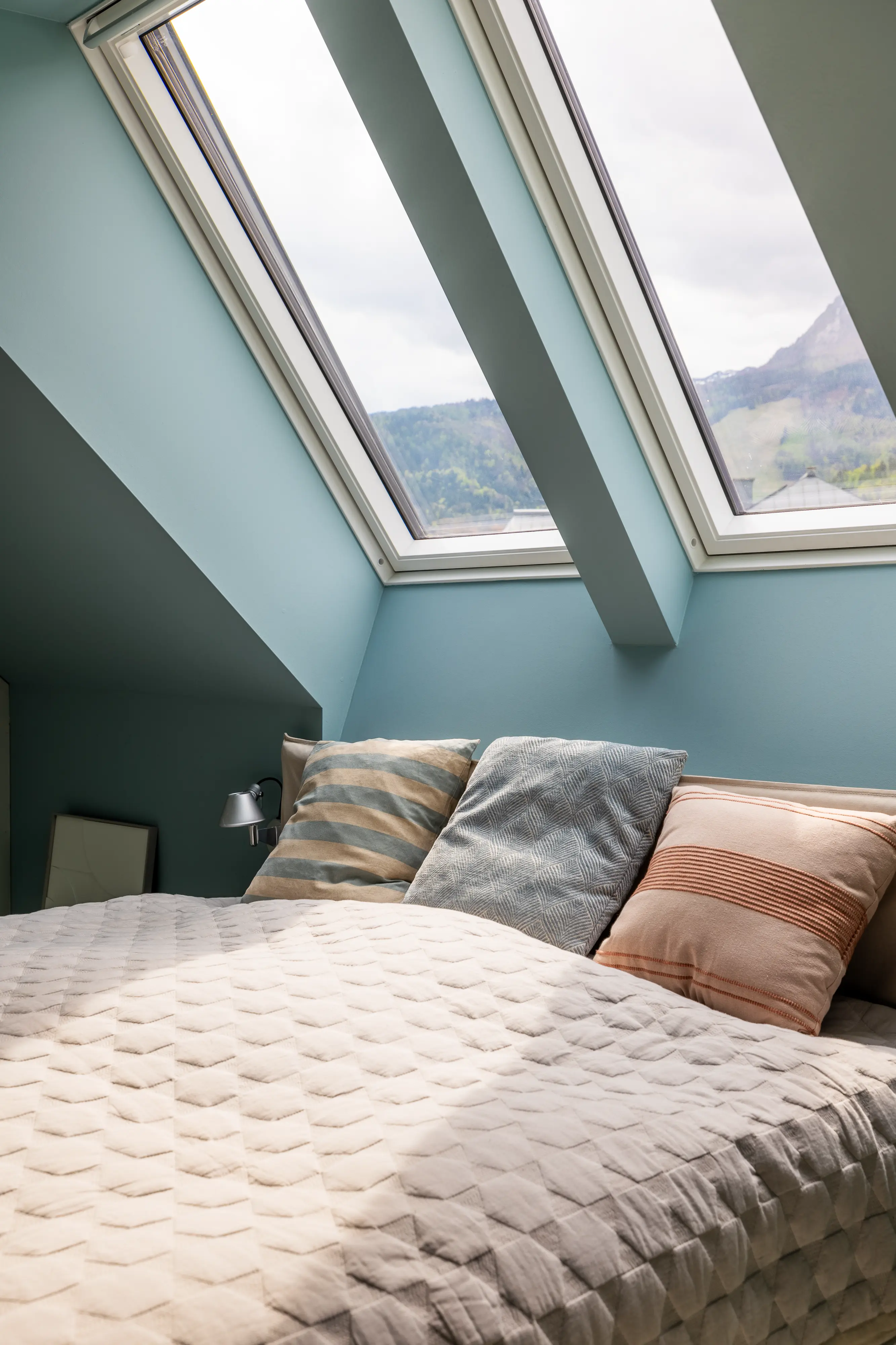 Palėpės miegamasis su nuožulniomis lubomis ir VELUX stogo langais, vaizdu į kalnus.