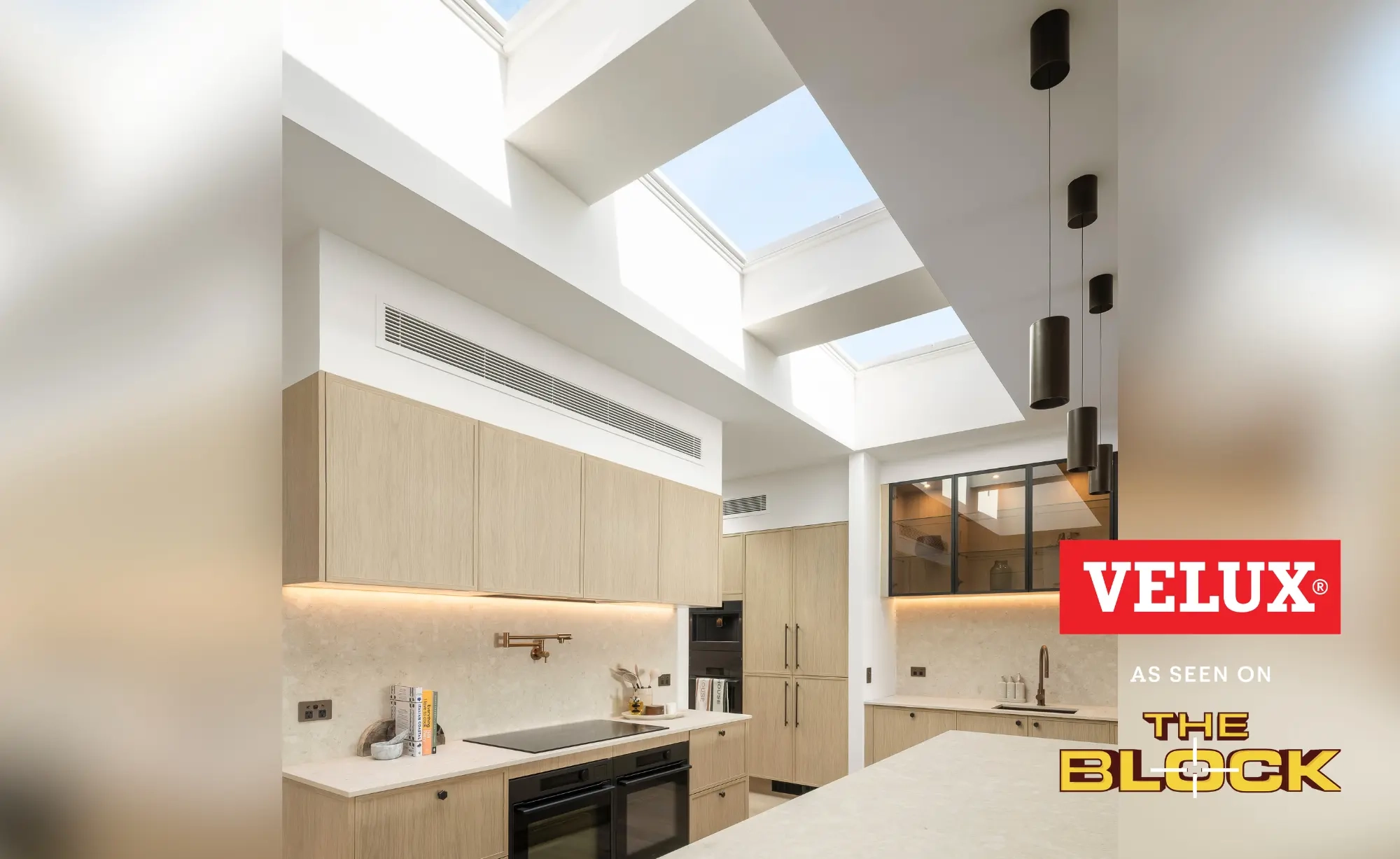 Modern kitchen lit by multiple VELUX flat roof windows above a light wood and stone interior.
