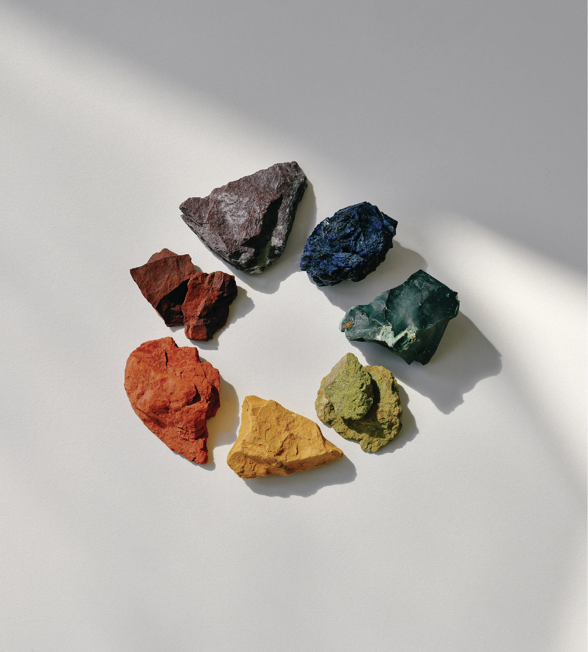Seven colorful mineral rocks arranged in a circle on a light surface.