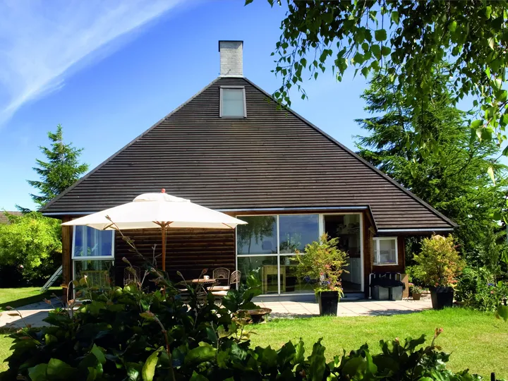Außenansicht eines Einfamilienhauses mit braunem Zeltdach, brauner Holzverkleidung, Terrasse und Garten | VELUX Magazin