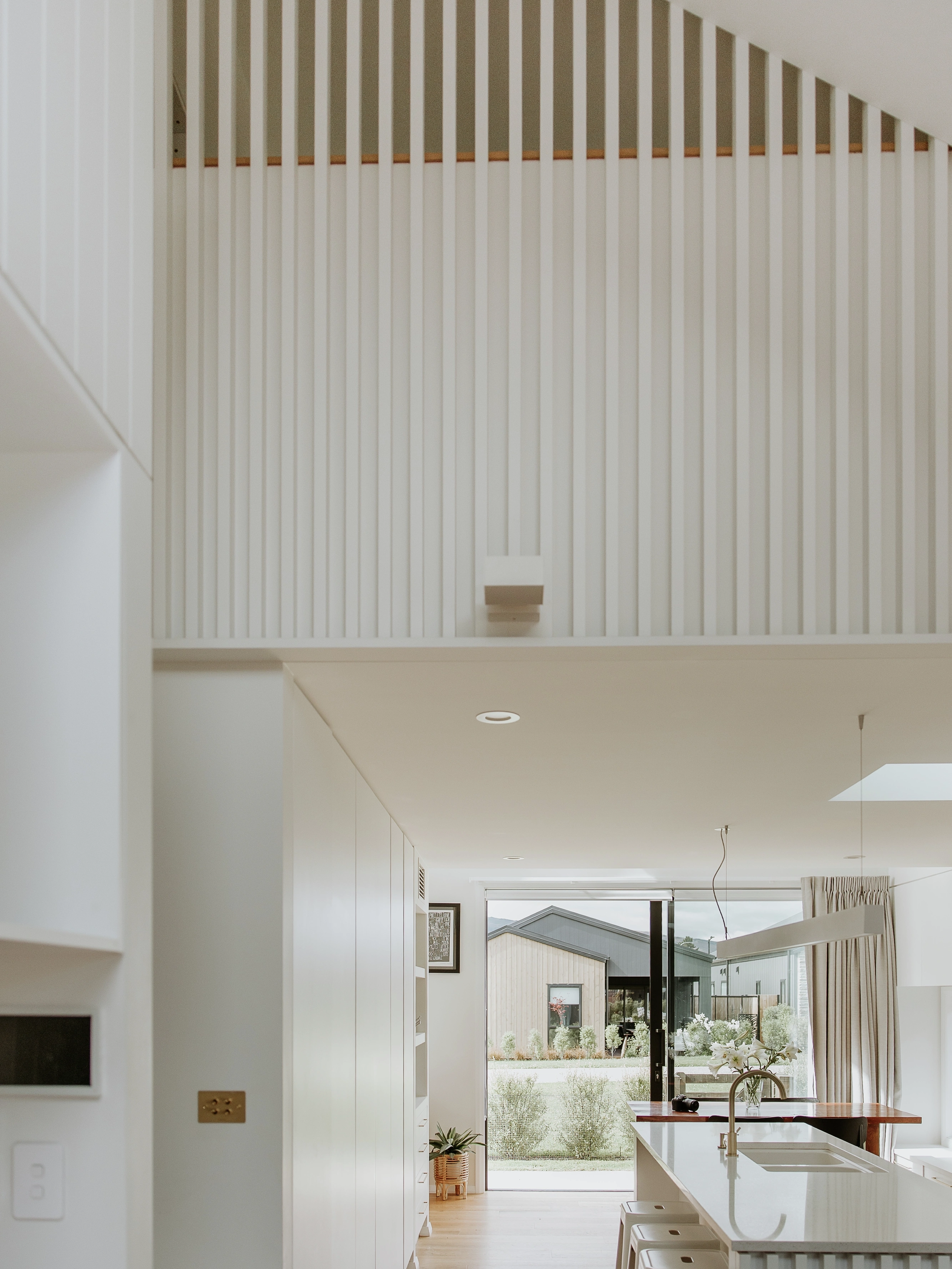 Minimal white kitchen with island and large glass doors opening to a green garden.