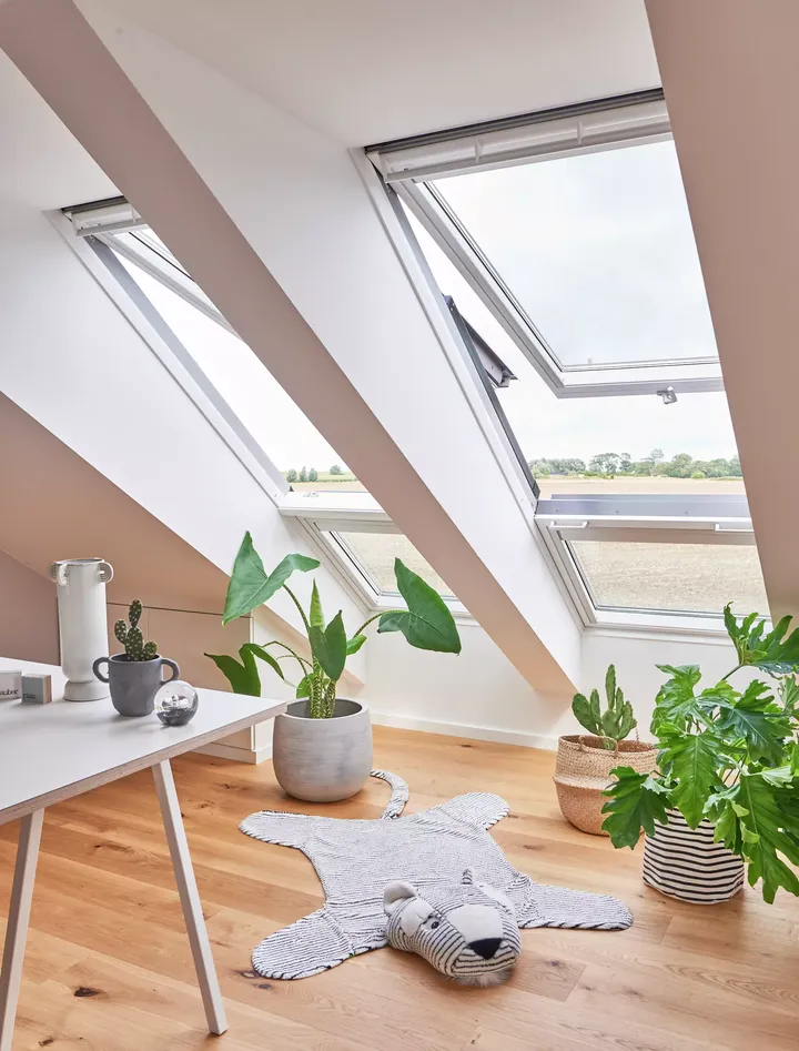 Gemütliches Dachboden-Homeoffice mit offenen VELUX Dachflächenfenstern und grünen Pflanzen.