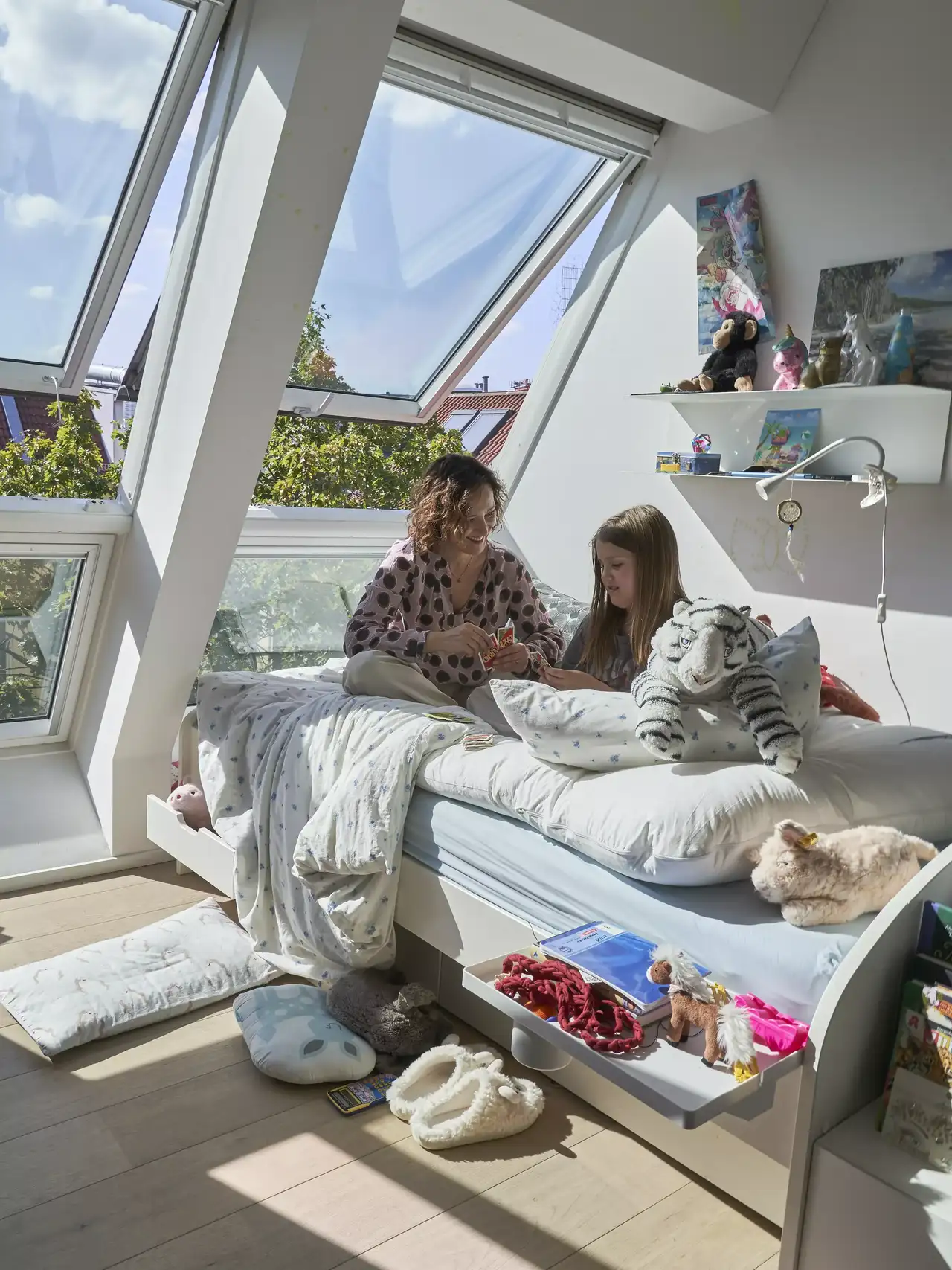 Frau faltet Wäsche während zwei Kleinkinder im Kinderbett unter dem Dachfenster spielen | VELUX Magazin