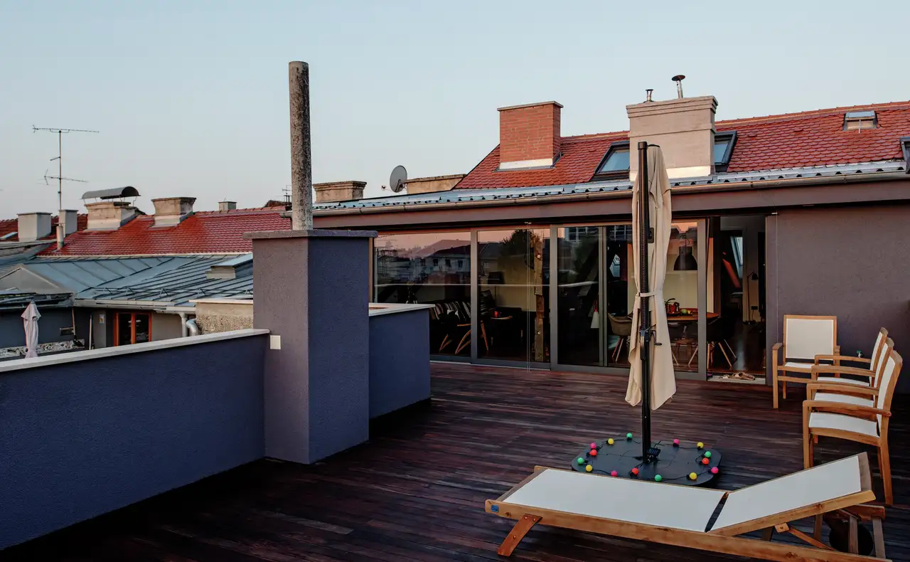 Une terrasse sur toit plat avec sol en bois, équipée de transats, fauteuils de jardin et d’un parasol fermé.