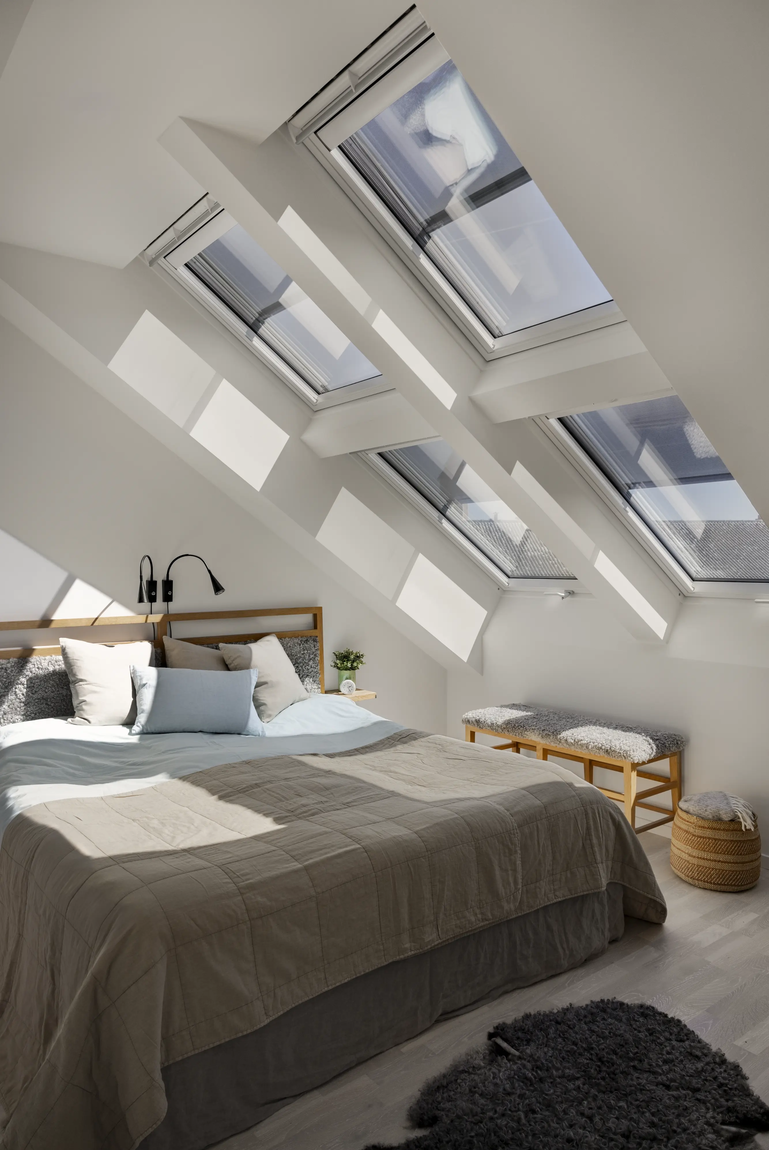 Világos tetőtéri hálószoba több VELUX tetőtéri ablakkal, amelyek bőséges természetes fényt engednek be, világosabbá és tágasabbá téve a pihenésre kialakított teret.