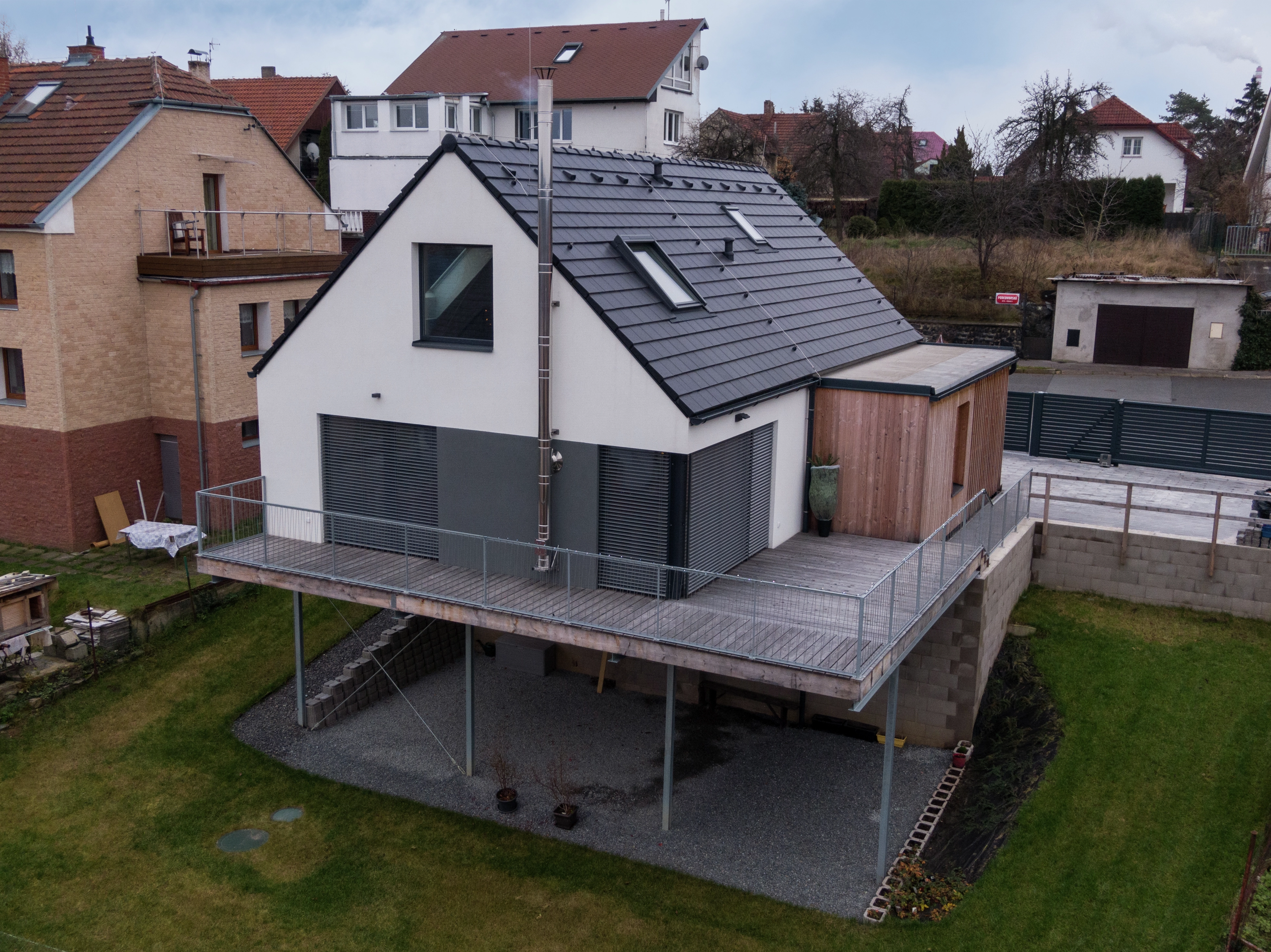 Modern house with dark tiled roof and elevated wooden deck in suburban area.
