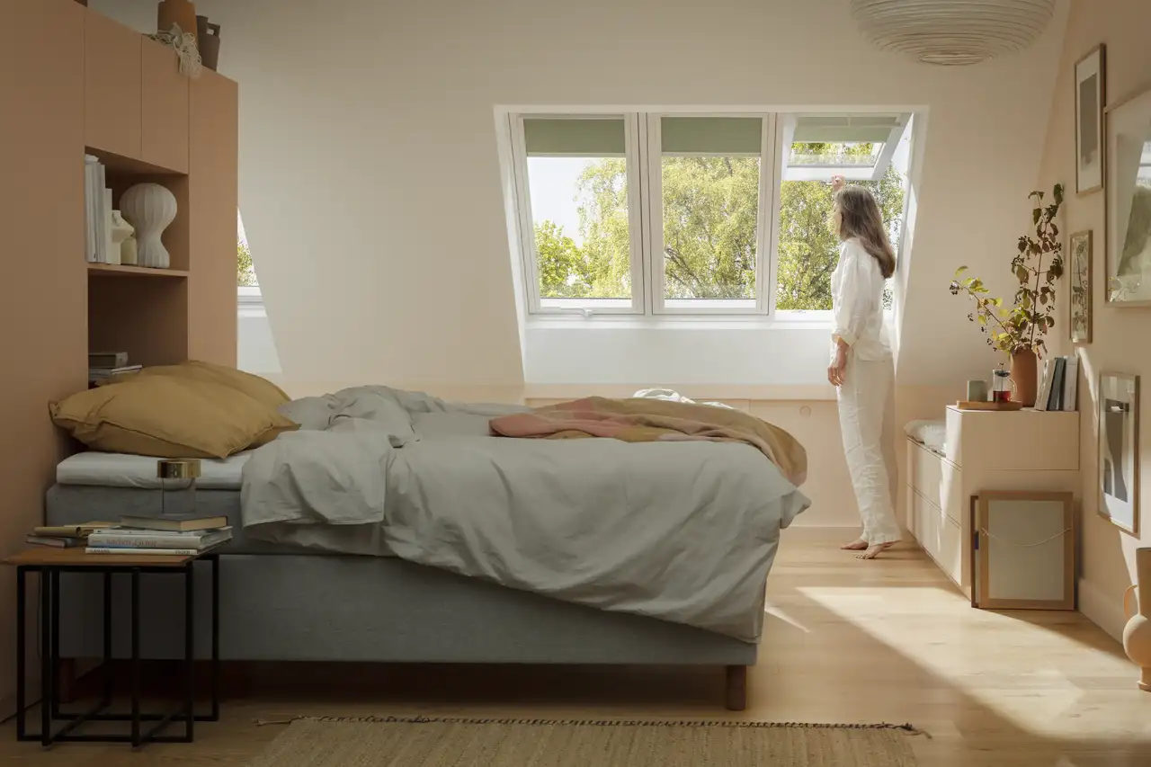 Attic bedroom with sloped ceiling and large VELUX 3in1 roof windows, natural light entering.