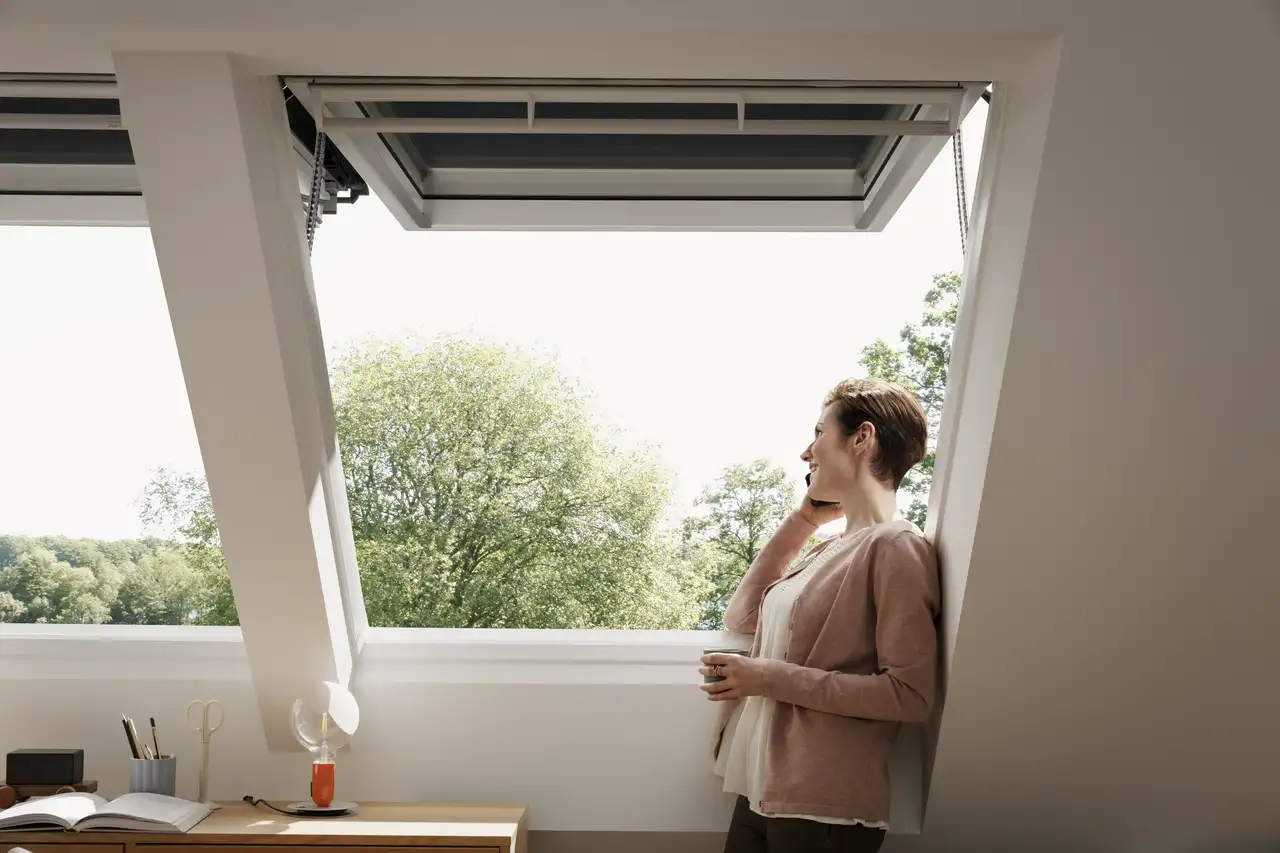 Kobieta rozmawia przez telefon i patrzy na zewnątrz przez okno dachowe VELUX.