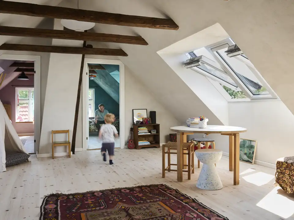Open space in mansarda con finestre per tetti VELUX, tavolo con sedie e tenda giocattolo per bambini