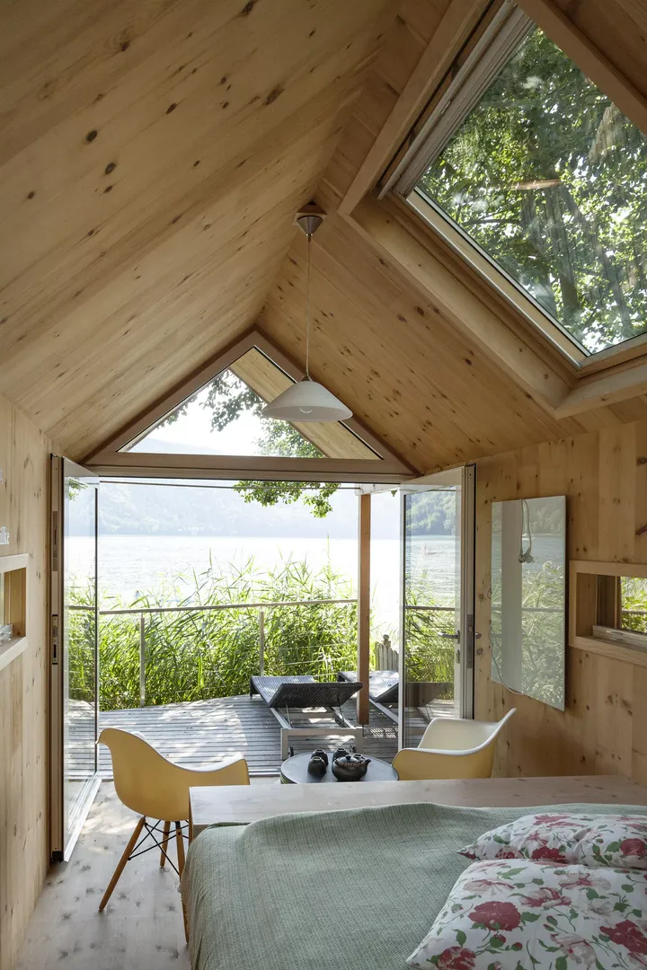 Gemütliches hölzernes Schlafzimmer mit VELUX Dachflächenfenster, das zu einem Balkon mit Aussicht auf den See führt.
