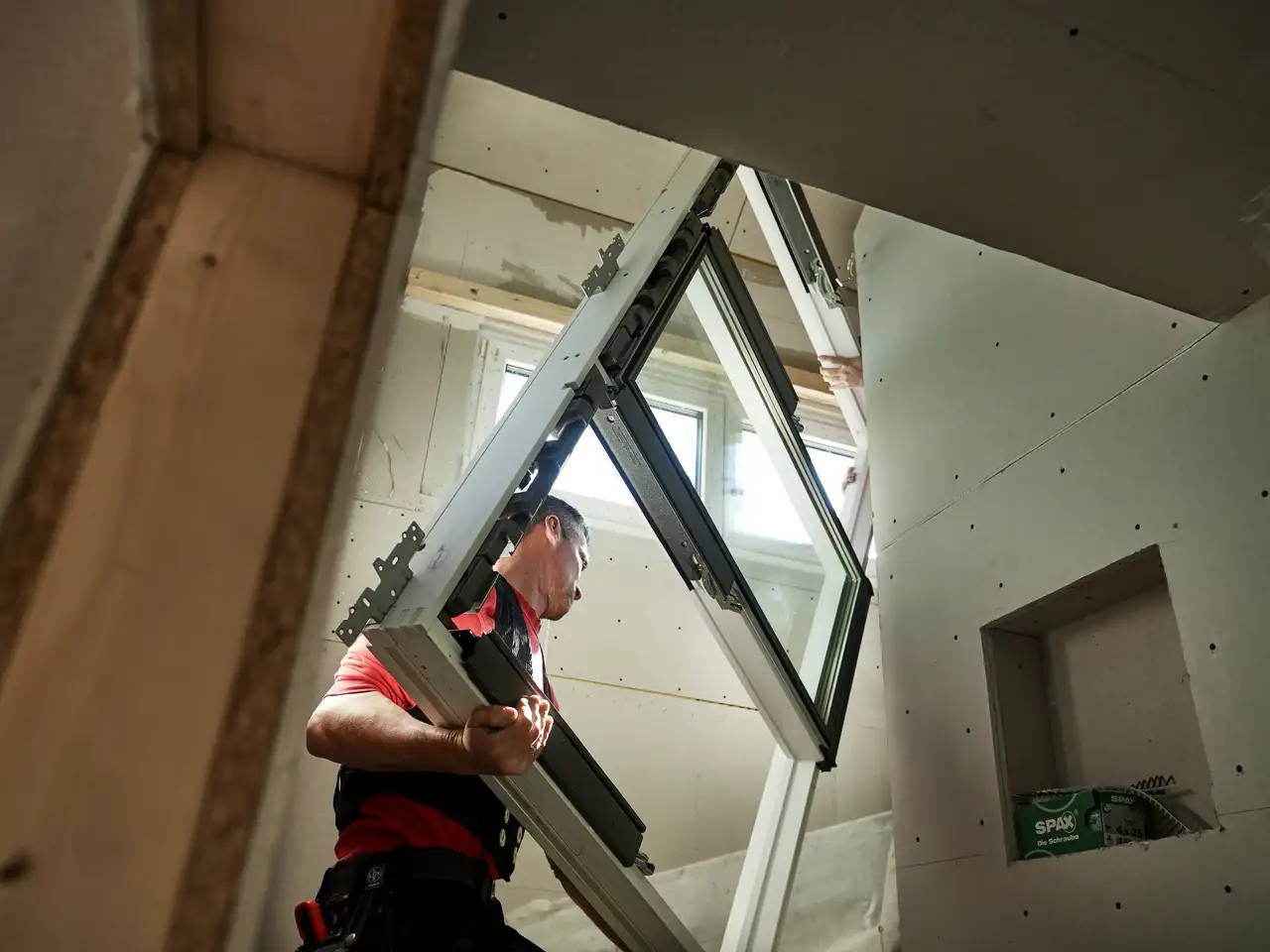 Dachdecker trägt ein Dachfenster die Treppe eines Rohbaus hoch | VELUX Magazin