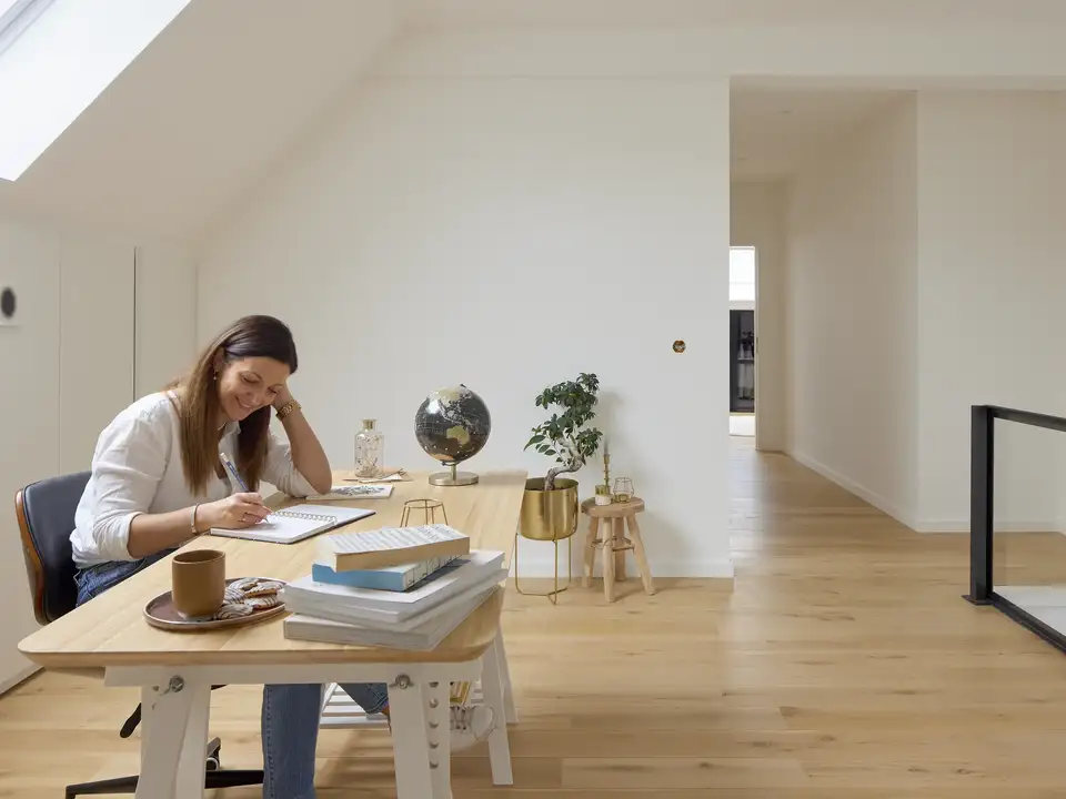 Zolder-thuiskantoor met schuine plafonds en VELUX dakraam, lichte werkruimte.