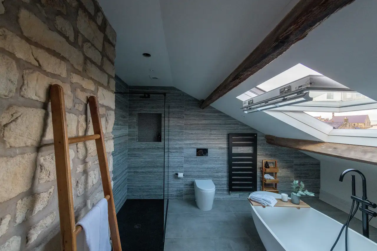 Eğimli tavanlı, VELUX pencereli ve modern armatürlü çatı katı banyosu  