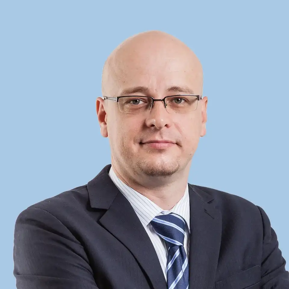 Man in a dark suit with a striped tie against a blue background.