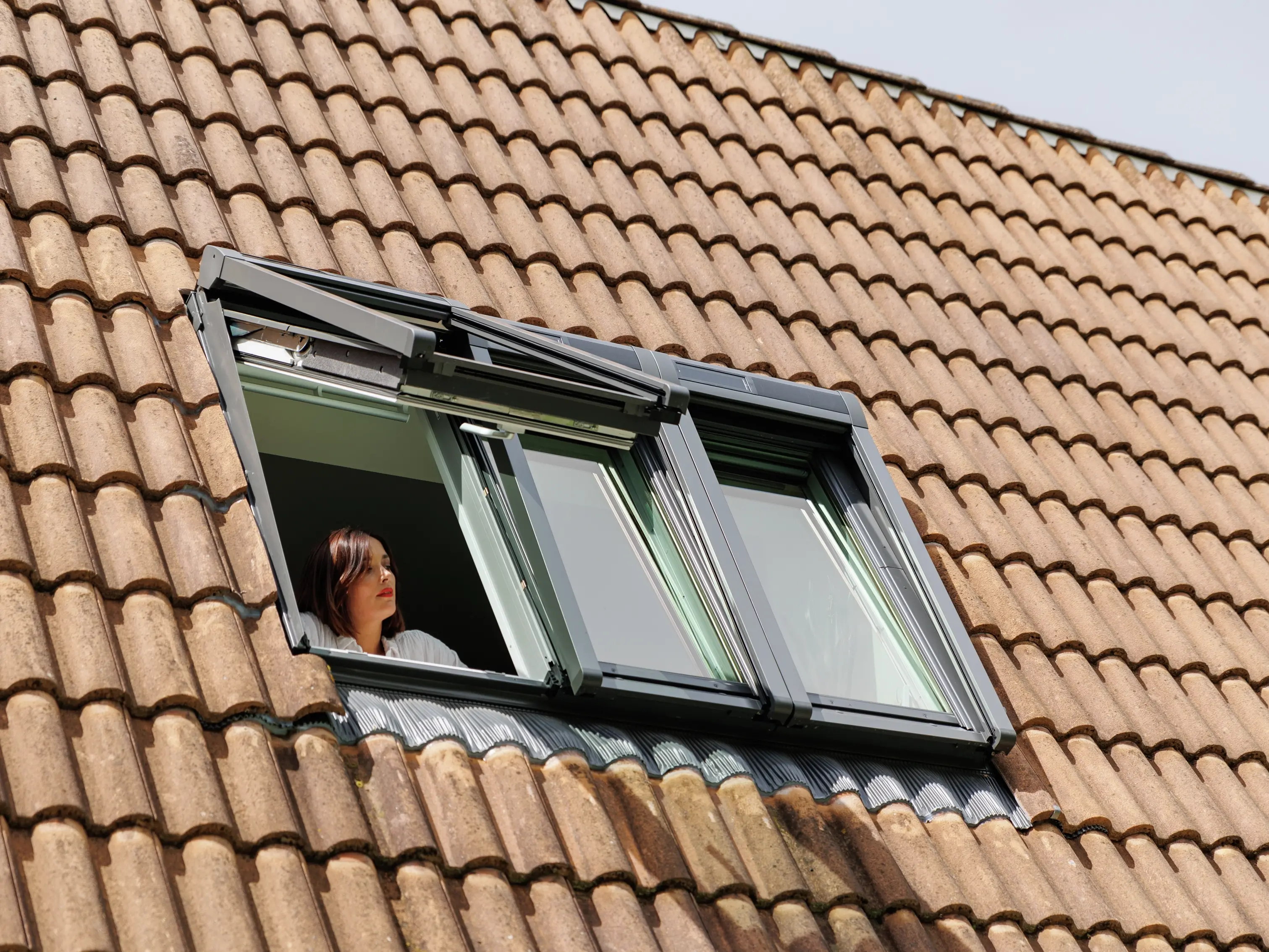 Une fenêtre de toit VELUX sur un toit en tuiles, ouverte vers le ciel.