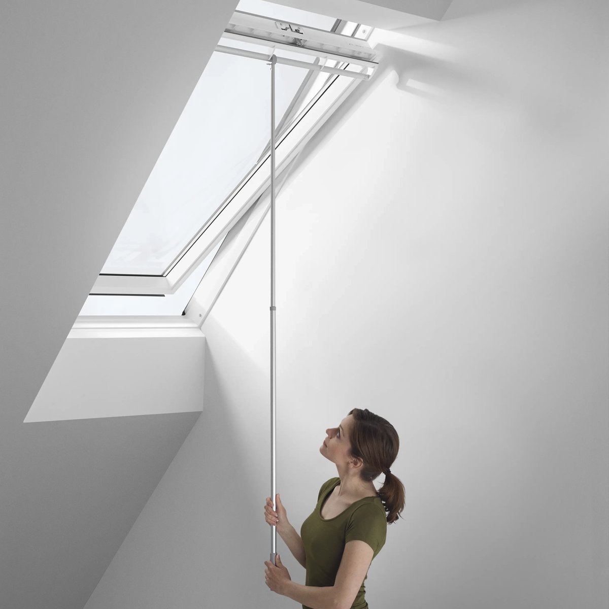 Person using a pole to open a VELUX roof window in a sloped ceiling room.