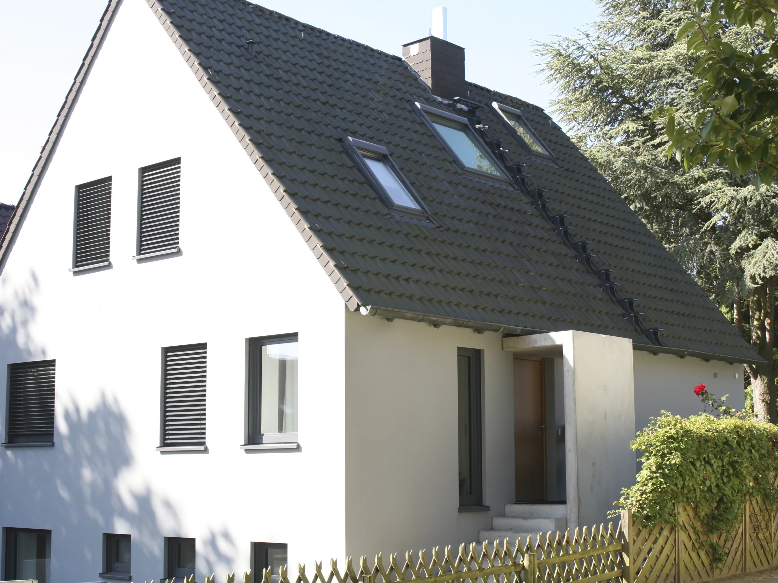 Maison moderne avec toit en pente et fenêtres de toit VELUX, entourée de verdure